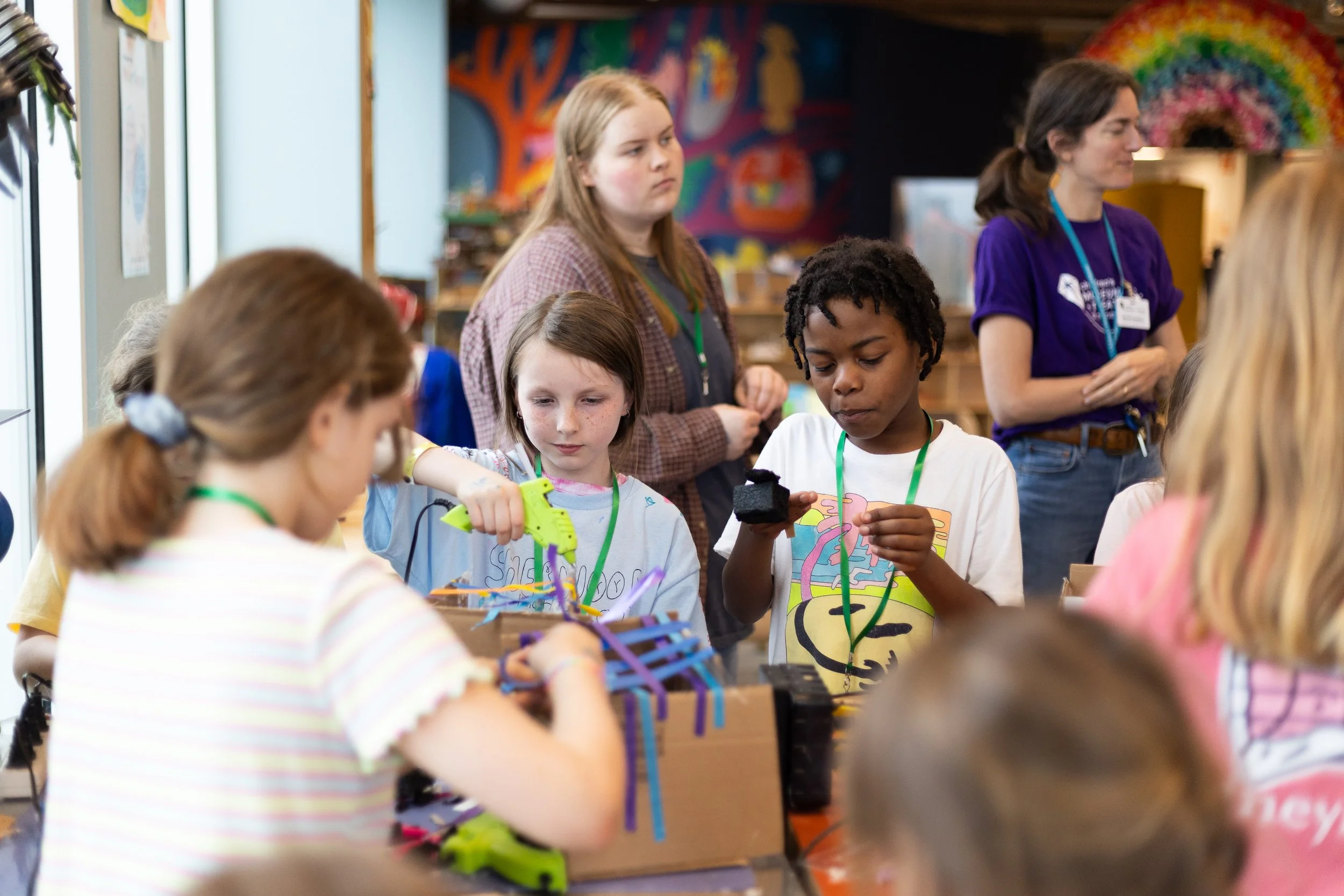 Several young children work on creative projects while teenage counselors stand in the background