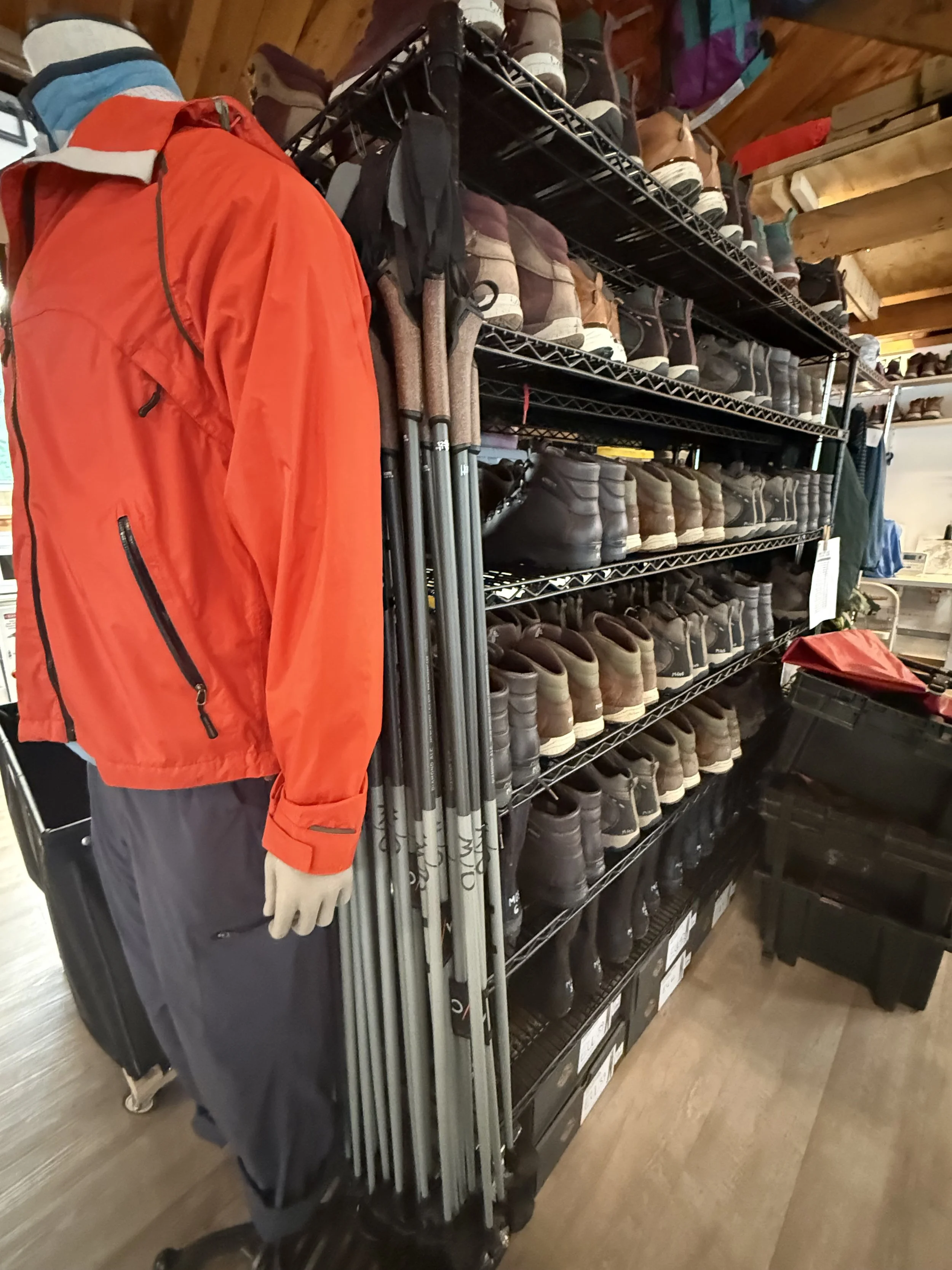A shelf of boots, ski poles, and a manequin in a jacket inside a gear library