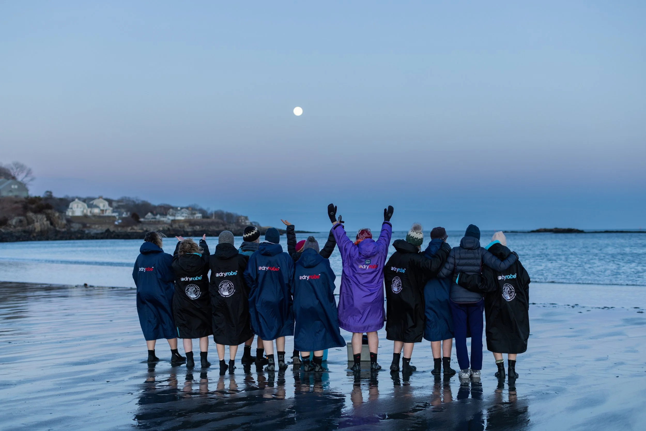 A group of 10 women triumphantly gather at the oceanfront during a full moon