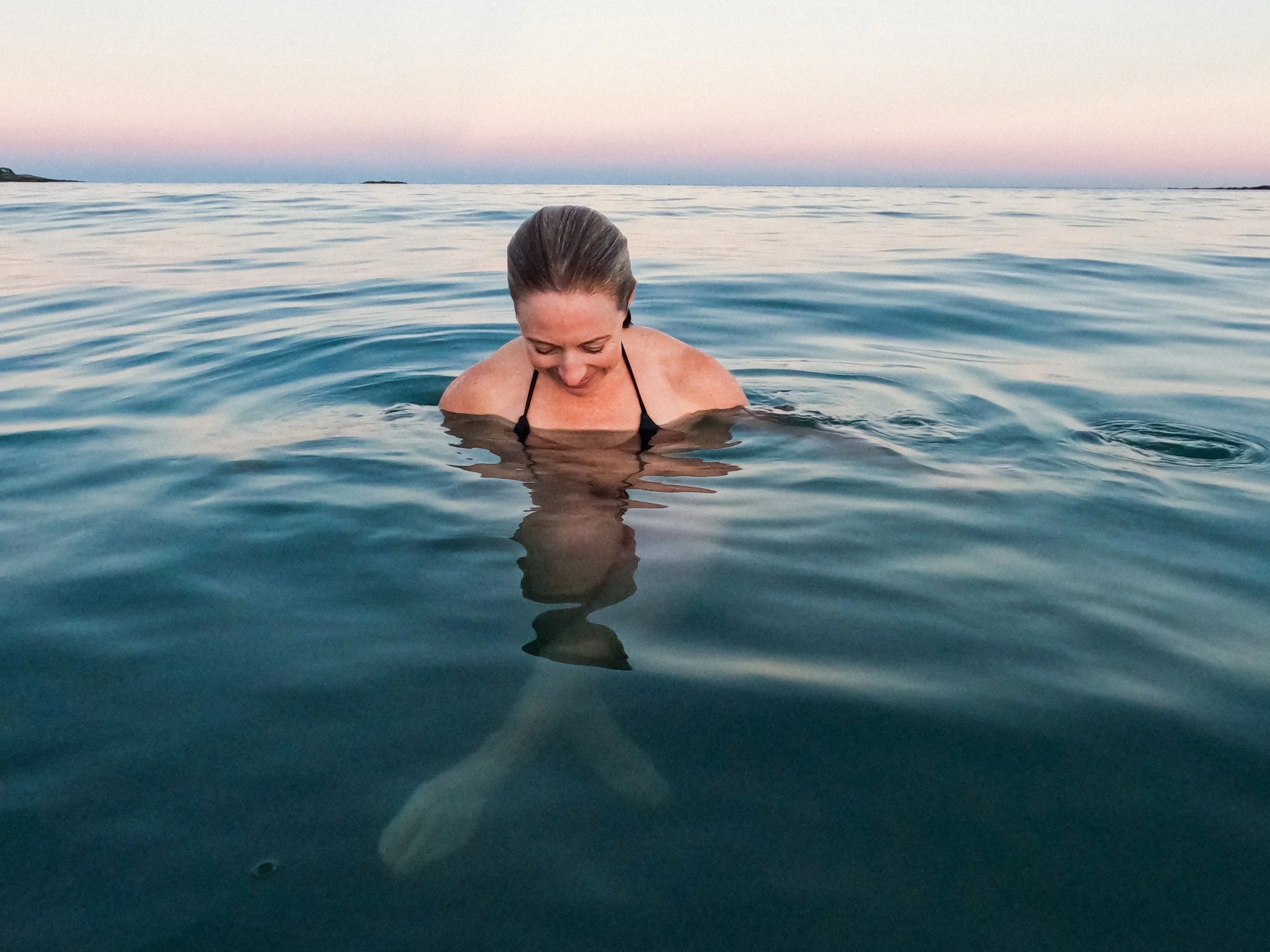 Woman in bathing suit immersed up to her shoulders in a coldwater plunge