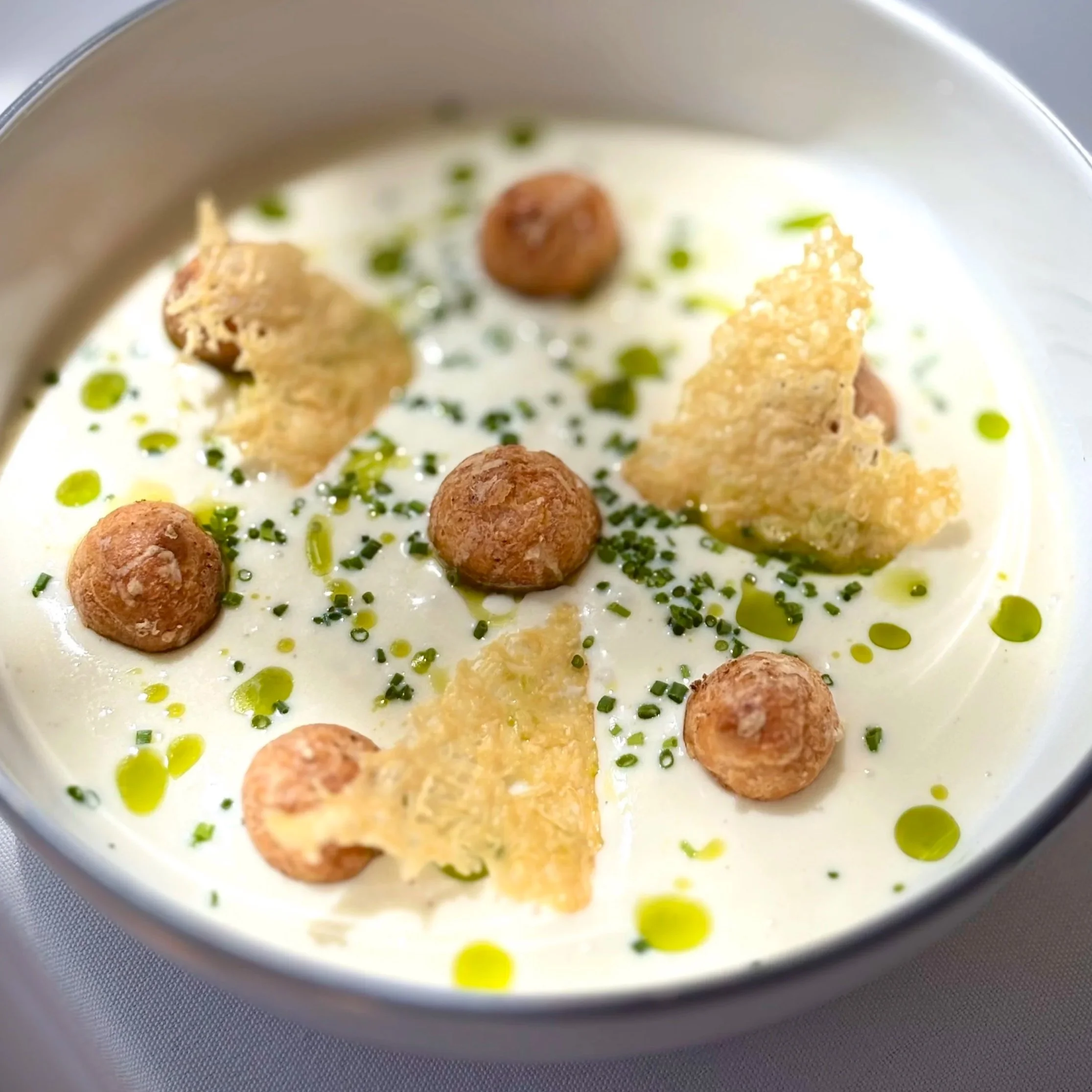 Image of Vichyssoise at Perle Restaurant - Chilled leek and potato soup, Parmigiano Reggiano crisps, gougères, chives