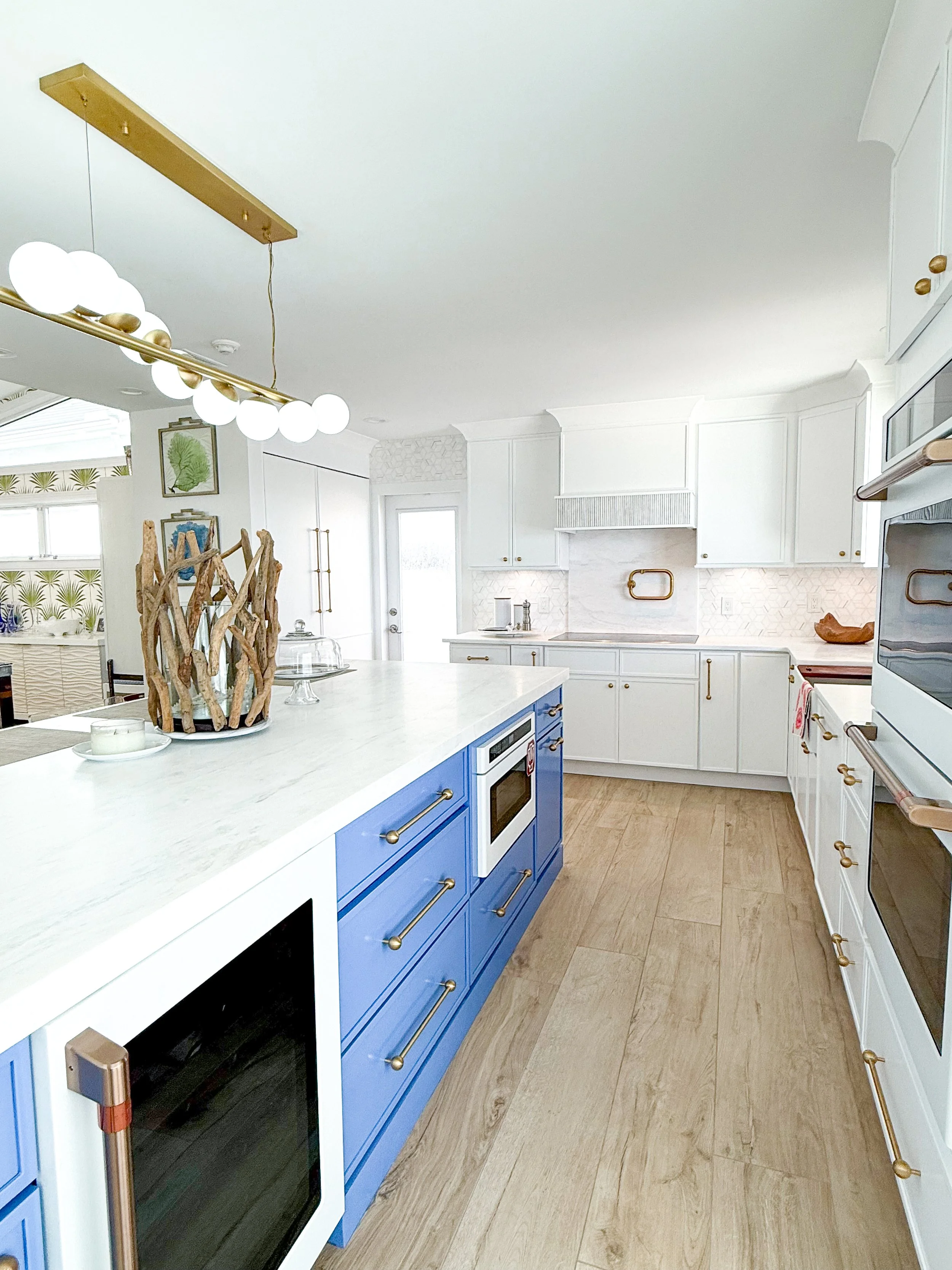 Bright kitchen with white cabinetry, a large blue island with gold handles, wood flooring, and modern appliances.