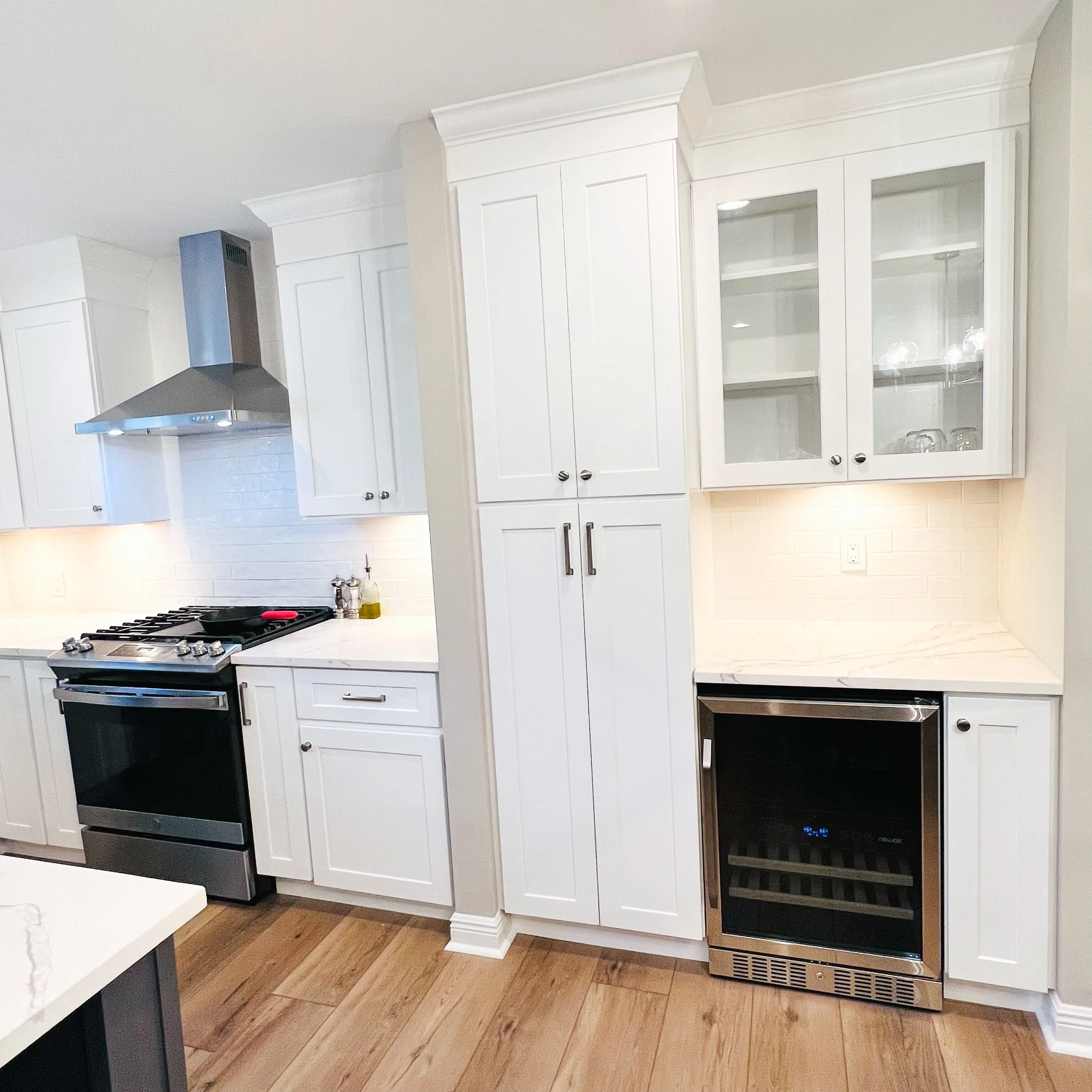 White kitchen cabinets with a stainless steel wine cooler, marble countertops, and hardwood floors.