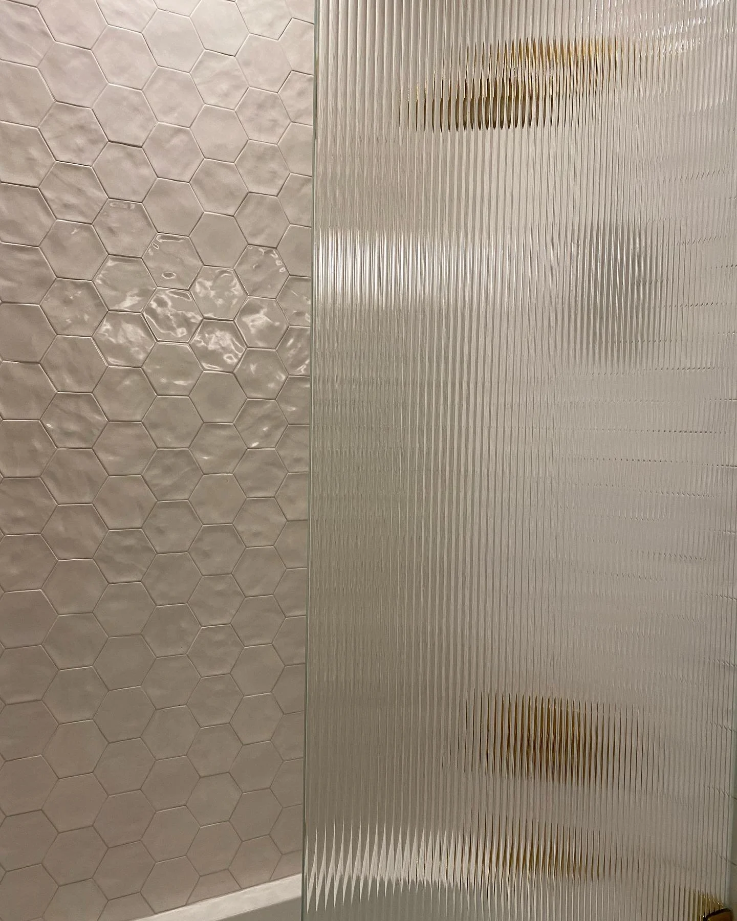 A bathroom wall with beige hexagonal tiles on the left and a textured frosted glass or plastic partition on the right.