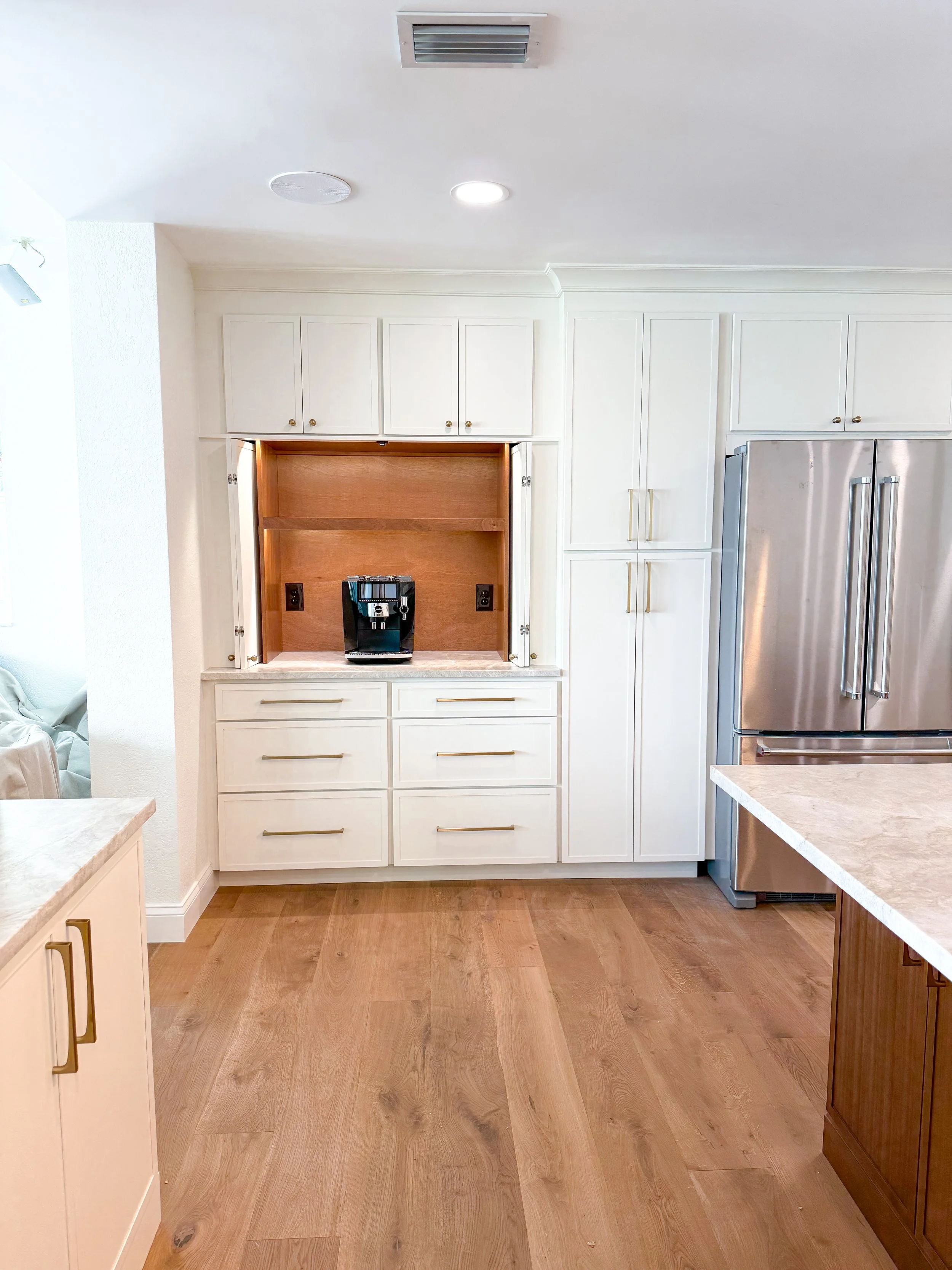 Kitchen with white cabinets, a stainless steel refrigerator, a coffee maker on a counter, and wood flooring.