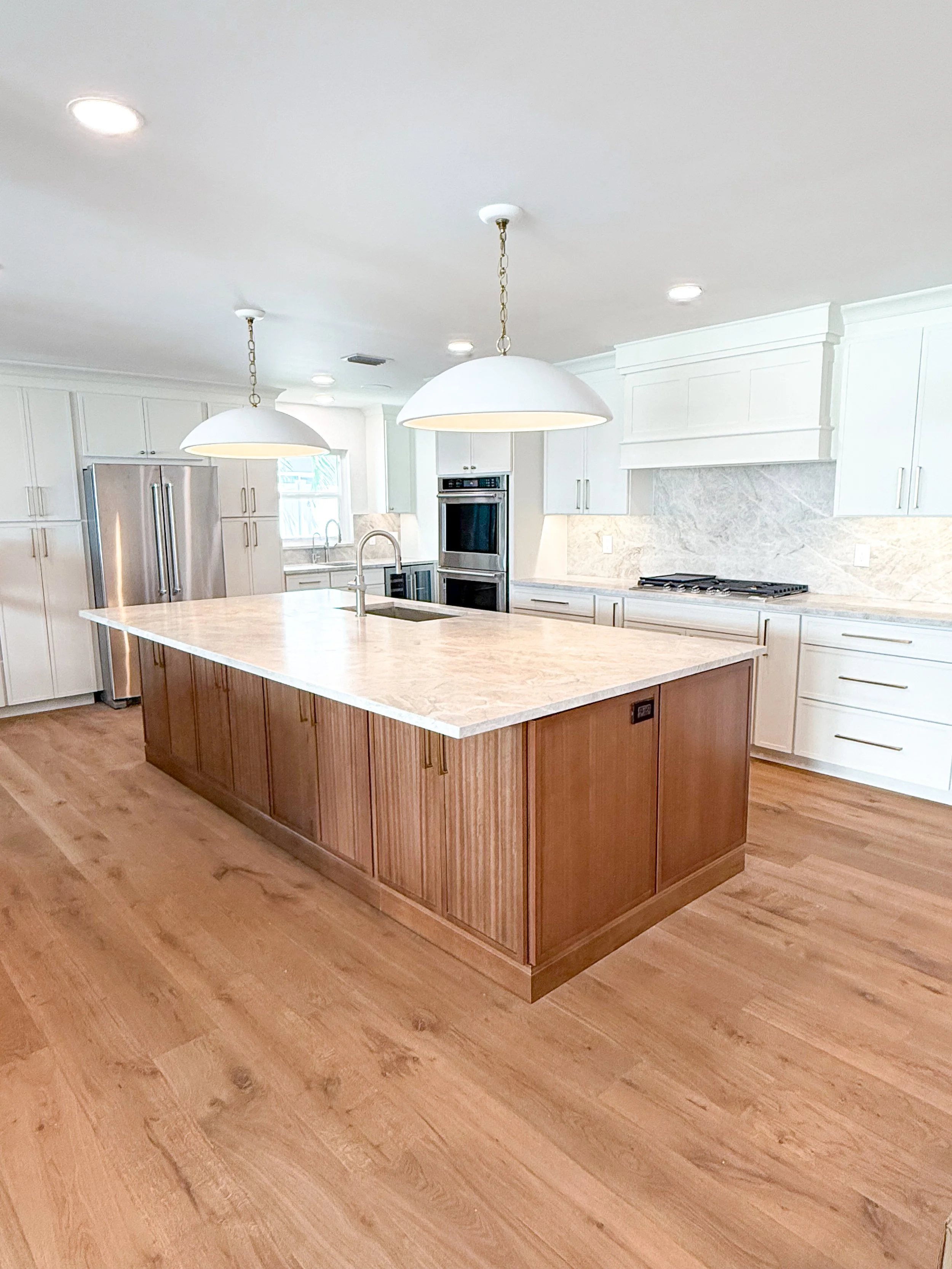 Modern kitchen with a large island, white cabinets, stainless steel appliances, and wooden flooring.