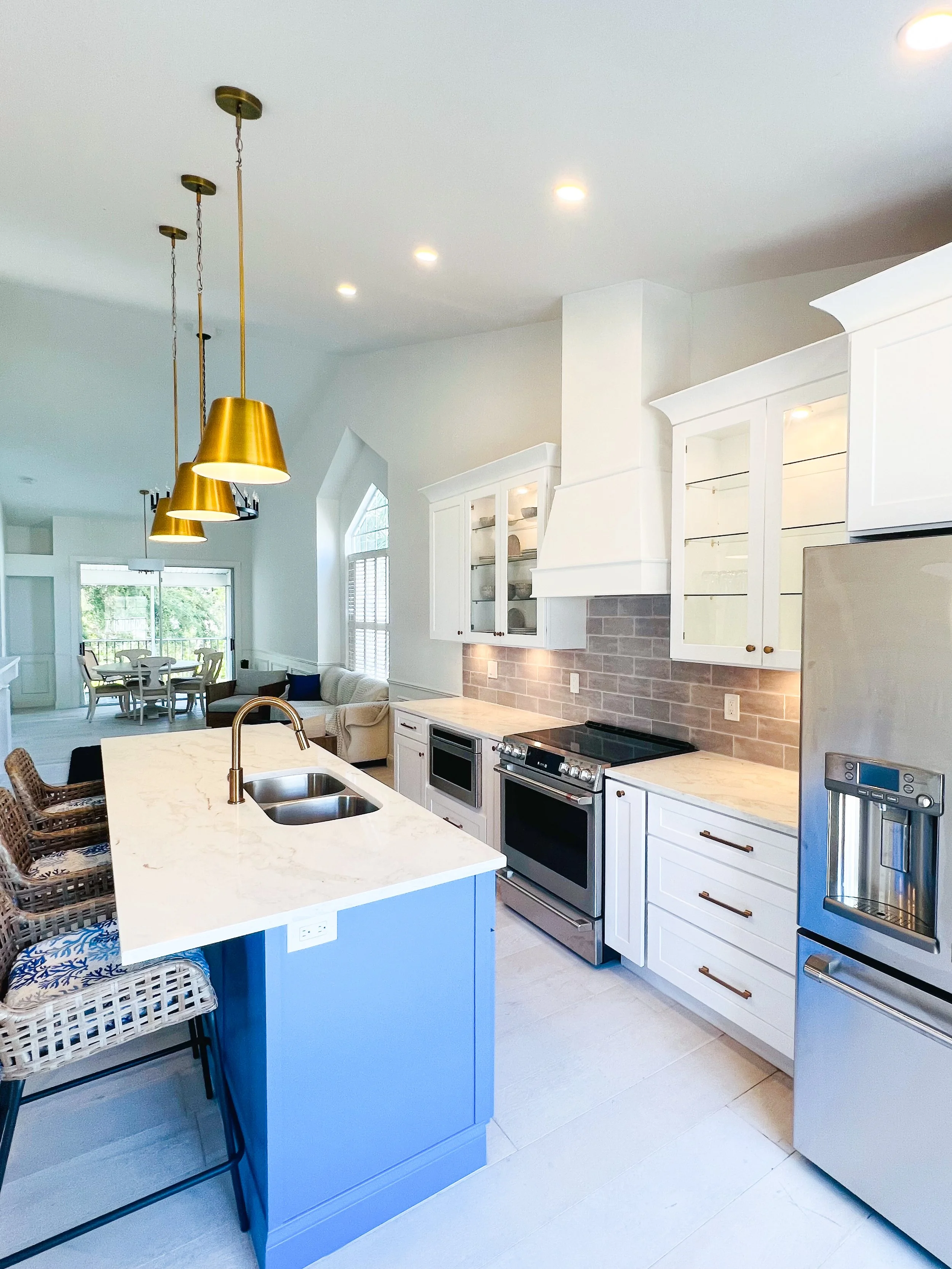 Modern kitchen with white cabinets, stainless steel appliances, a marble island with a double sink, and gold pendant lights.