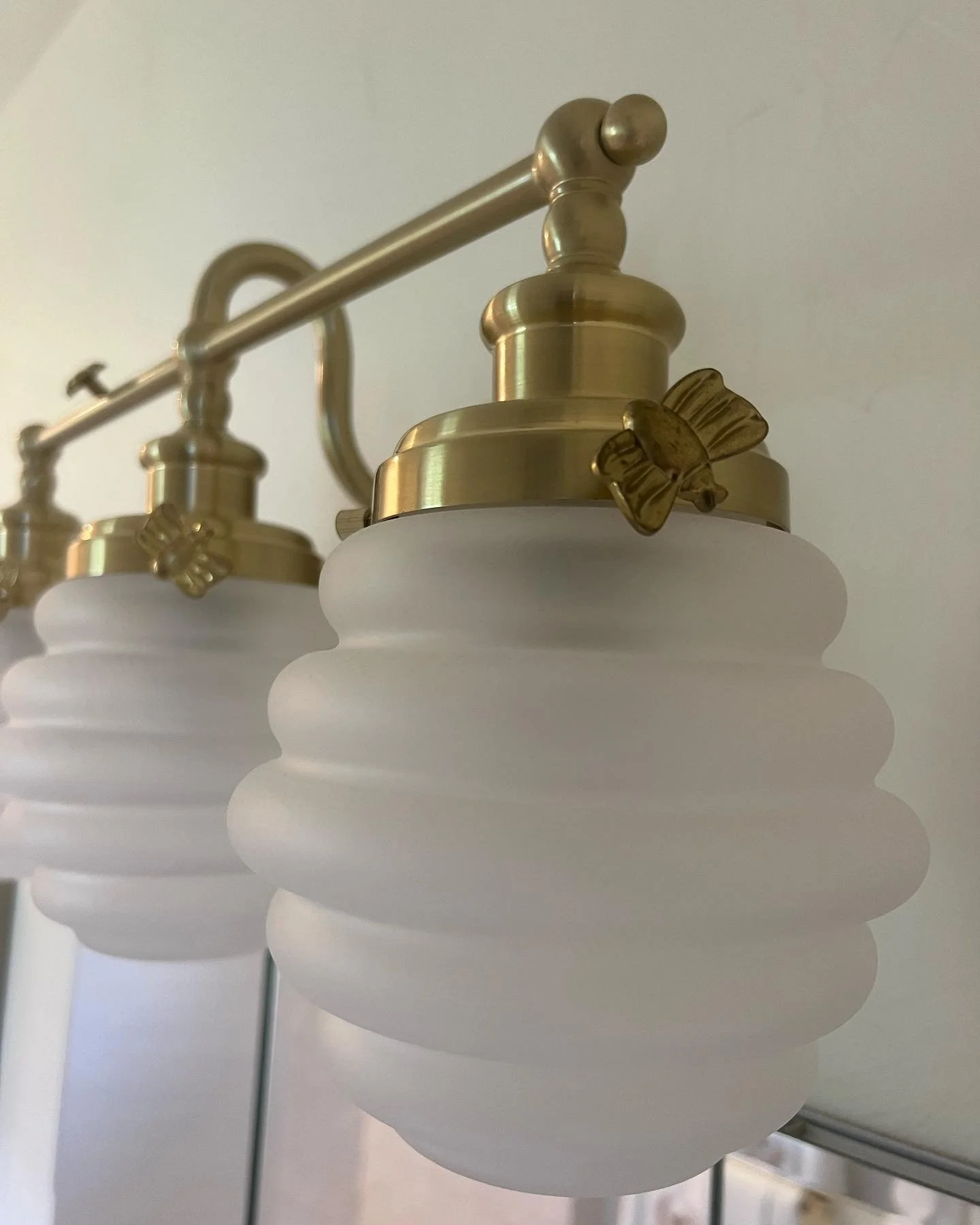 Close-up of vintage brass and frosted glass bathroom vanity lights with decorative bows.