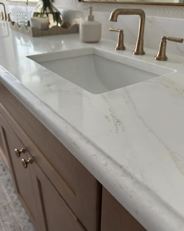 Close-up of a white marble countertop with an undermount sink, brass faucet, and wooden cabinet.