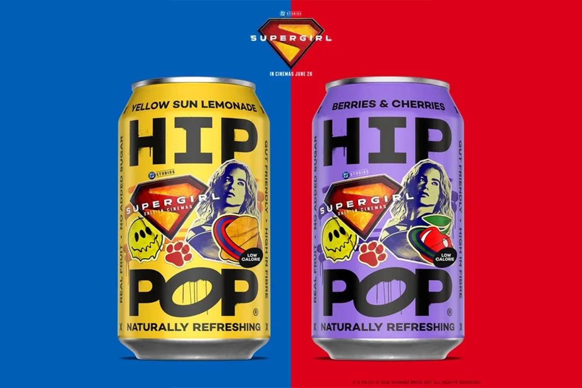 Limited-edition HIP POP x Supergirl cans featuring Yellow Sun Lemonade and Berries & Cherries flavours, showcasing bold comic-inspired packaging and colourful branding against contrasting blue and red backgrounds.