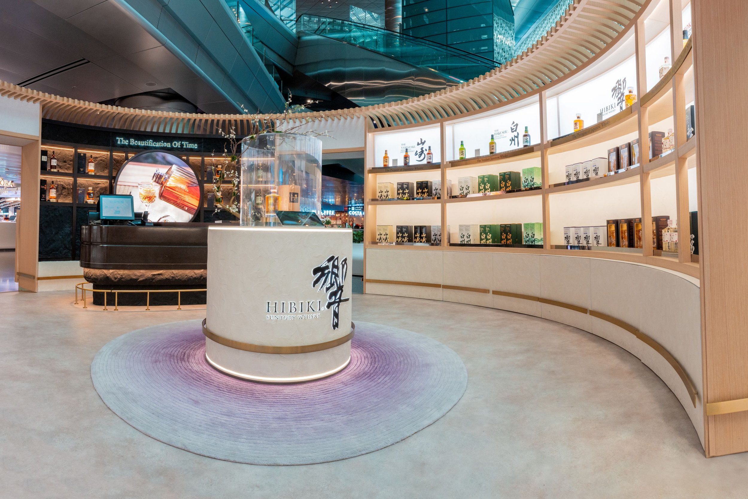  Premium Hibiki Japanese whisky display in a modern airport retail space featuring curved shelves with elegant bottles, a central showcase, and contemporary architectural design. 