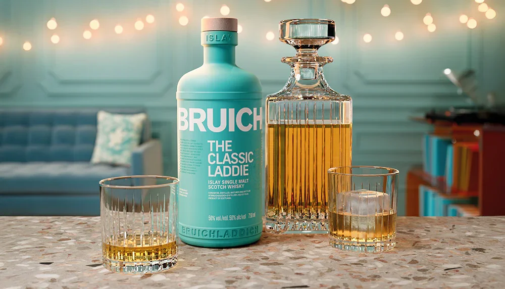  Bruichladdich The Classic Laddie Islay Single Malt Scotch Whisky bottle displayed with a crystal decanter and two whisky glasses on a terrazzo countertop in a stylish setting with warm festive lights. 
