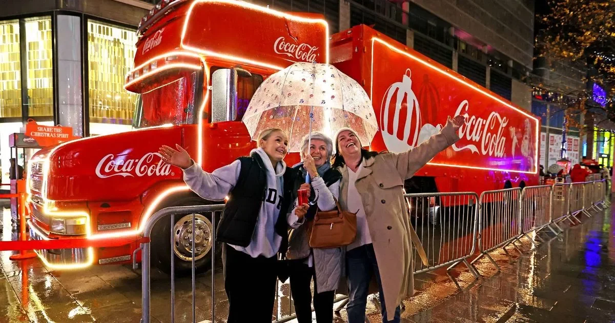  Iconic Coca-Cola Christmas truck illuminated with festive lights on a rainy evening, surrounded by holiday decorations and visitors enjoying the seasonal celebration in a vibrant city setting. 