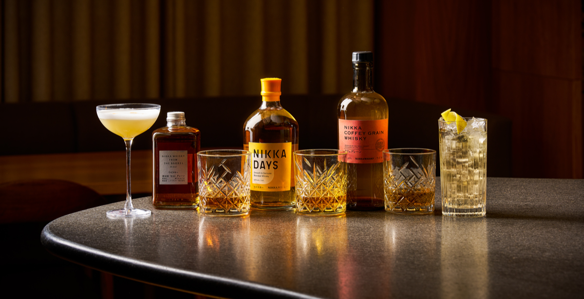  Nikka Whisky x Sticks ‘n’ Sushi bar display featuring Nikka Days and Nikka Coffey Grain bottles, crafted cocktails and whisky glasses arranged on a polished counter with warm, refined lighting. 