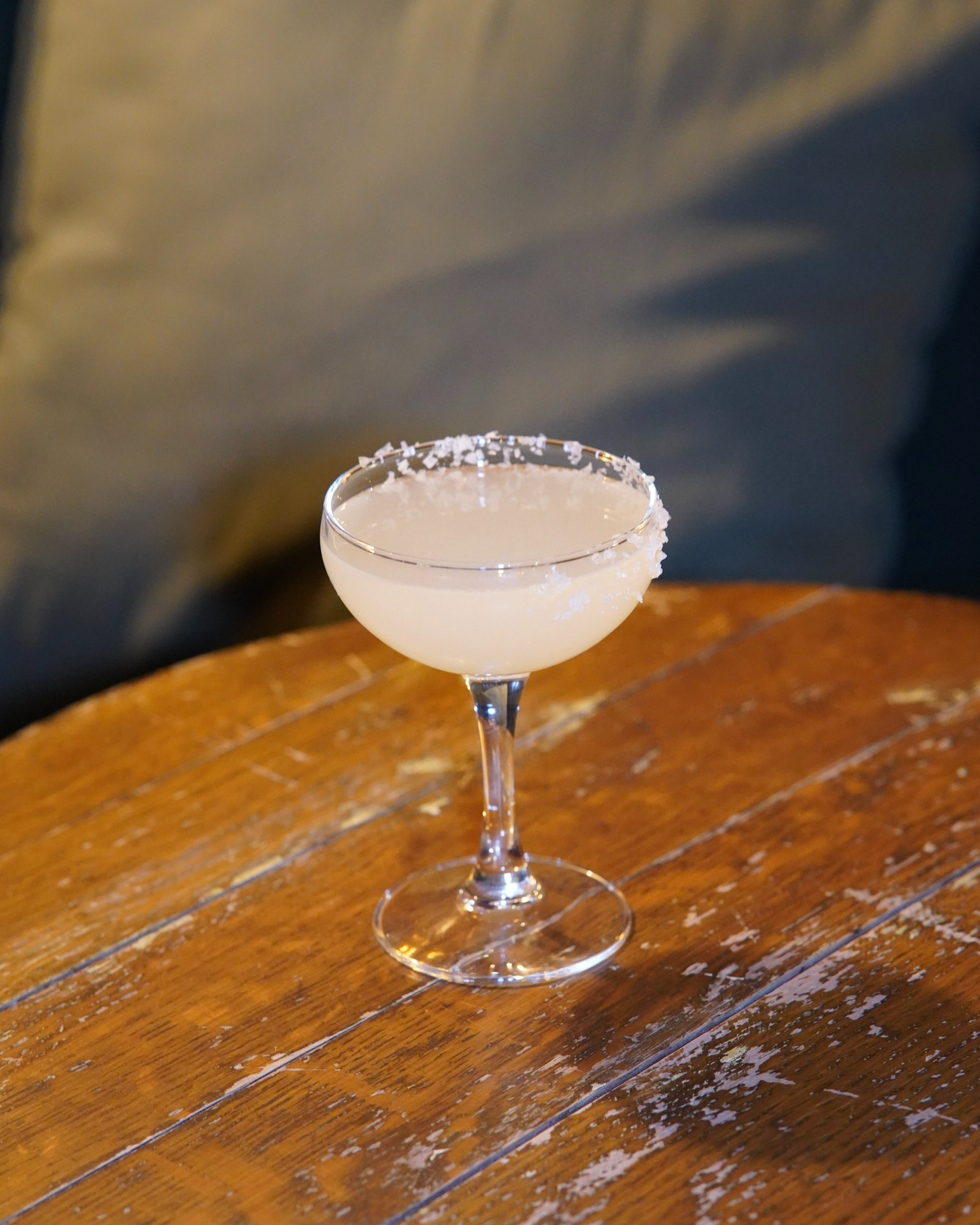  Classic margarita cocktail served in a coupe glass with a salted rim, placed on a rustic wooden table, highlighting fresh citrus tones and minimalist presentation. 