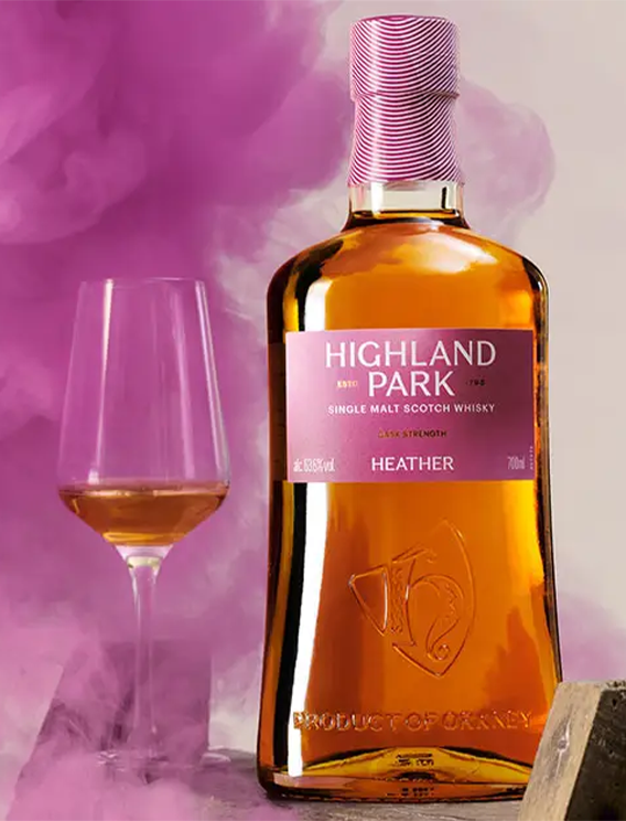  Highland Park Heather single malt Scotch whisky bottle displayed with a whisky glass against a smoky pink backdrop, highlighting the cask strength release, amber liquid and premium Orkney branding. 