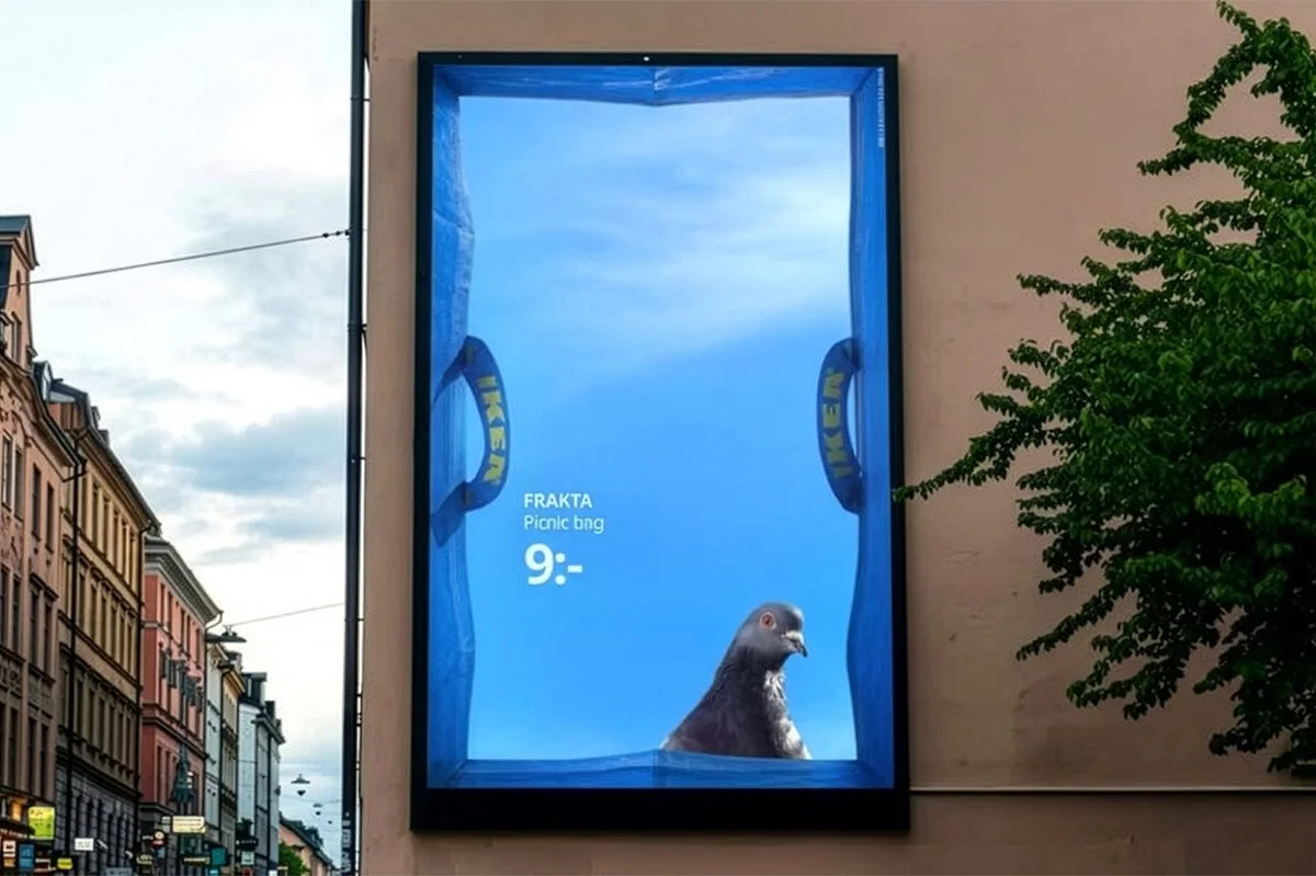  IKEA FRAKTA campaign billboard showing a pigeon inside a blue FRAKTA bag visual, displayed on a city street wall with surrounding buildings, highlighting the playful picnic bag concept priced at 9. 