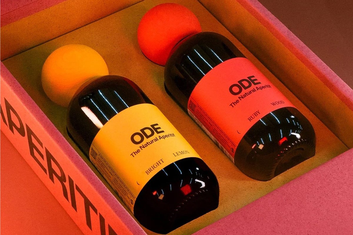  Two ODE natural aperitif bottles displayed in a branded box, featuring bold yellow and red labels labelled Bright Lemon and Ruby Wood, set against warm, vibrant lighting for a premium spritz and aperitivo aesthetic. 