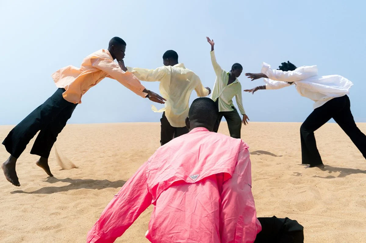  Photographic work from Delali Ayivi’s ‘Heimat (In Quarantine)’ series, featuring figures in pastel shirts moving across a sandy landscape, capturing cultural identity and movement through bold composition and colour.” 