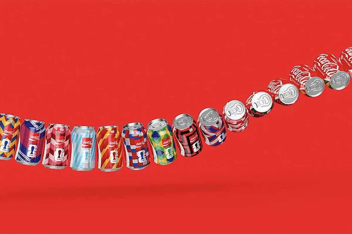  Lineup of limited edition Coca‑Cola FIFA cans in assorted colourful designs, arranged diagonally against a bold red background, showcasing collectible packaging for global football tournament branding. 