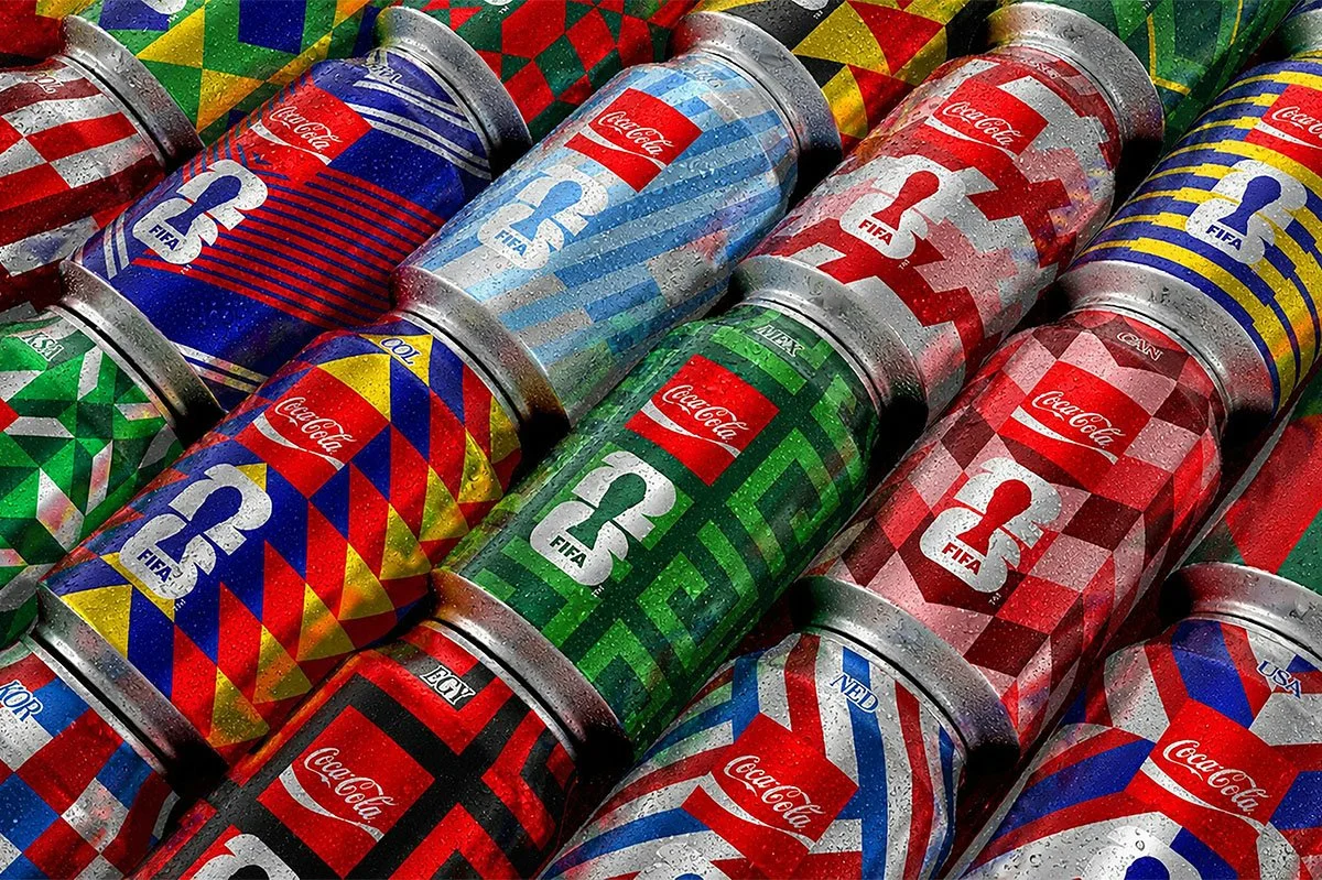 Close‑up of limited edition Coca‑Cola FIFA cans in vibrant geometric patterns, covered in condensation and arranged tightly together, showcasing colourful global football‑inspired packaging design.
