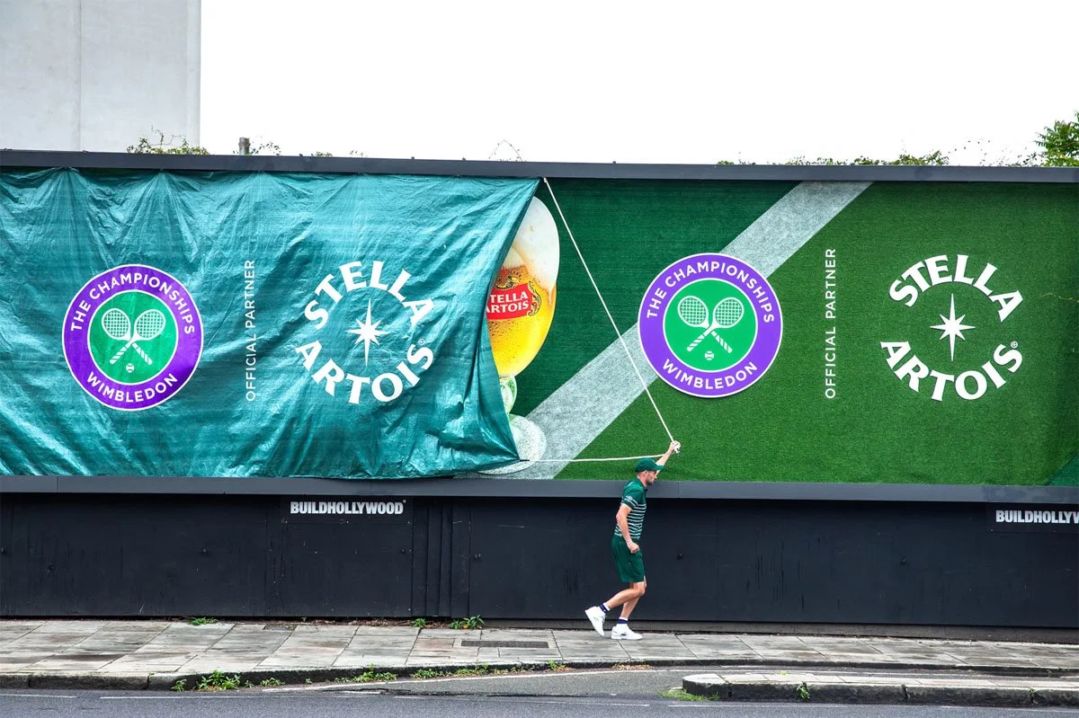 Stella Artois ‘When It Rains, We Pour’ campaign billboard near Wimbledon, featuring a tennis court design, branded rain cover reveal and official Championships partnership promoting beer consumption during wet weather. 