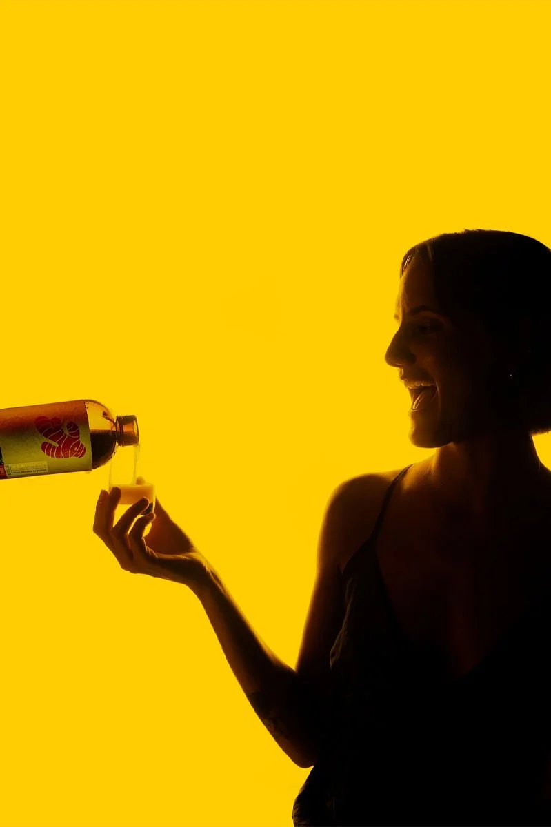  Silhouette of a person pouring Zázvorica fine ginger liqueur into a small glass against a vibrant yellow backdrop, highlighting the premium Slovak spirit’s distinctive ginger-inspired branding and contemporary presentation. 