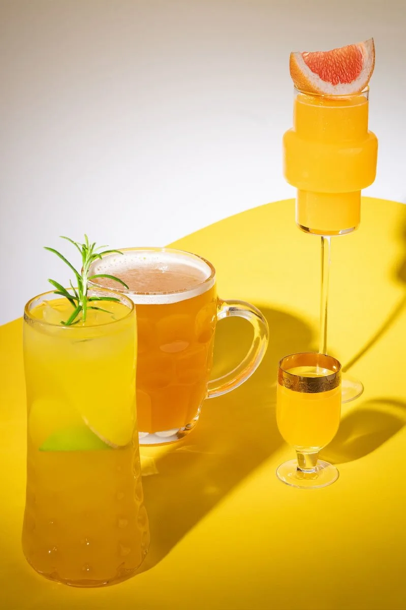  Selection of Zázvorica fine ginger liqueur cocktails served in distinctive glassware, featuring citrus garnishes and golden hues on a vibrant yellow tabletop, showcasing the versatility of the premium Slovak ginger spirit. 