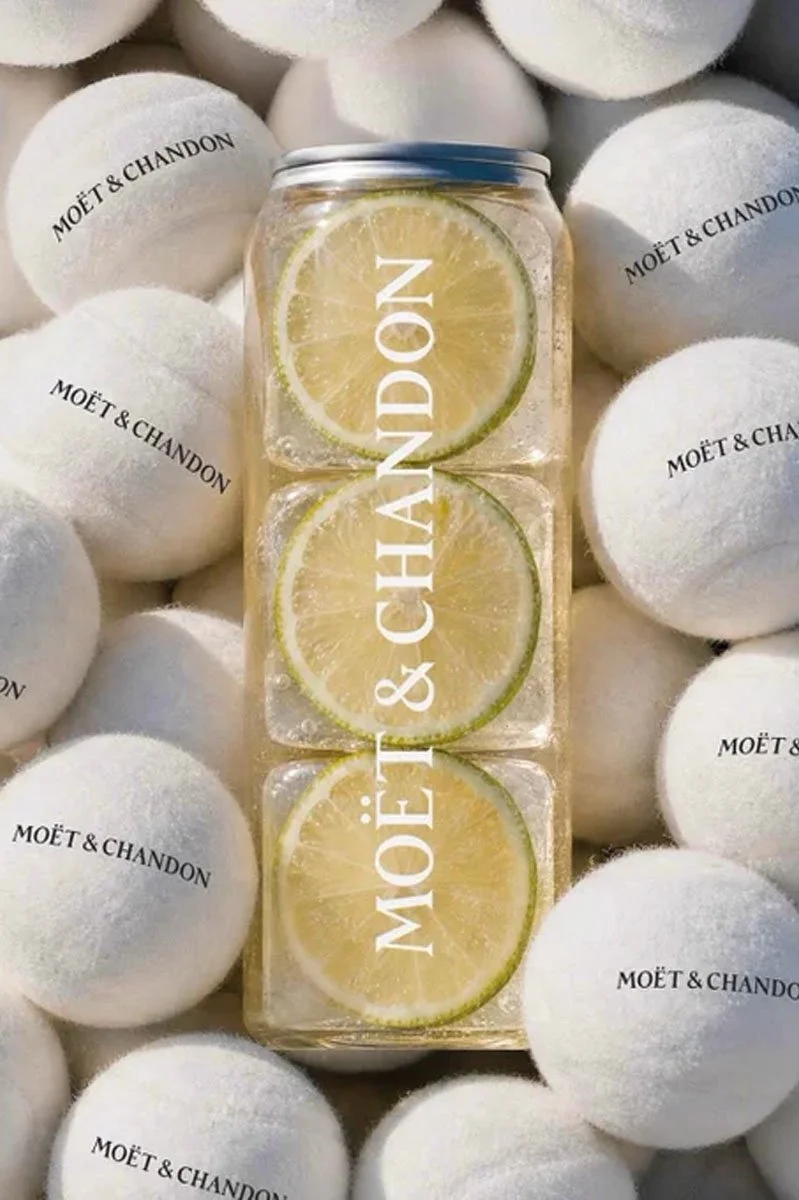  Moët &amp; Chandon Champagne-inspired canned serve surrounded by branded tennis balls and citrus slices, highlighting the luxury drinks brand’s US Open partnership and premium sporting occasion. 