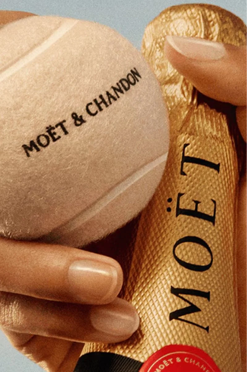  Close-up of a Moët &amp; Chandon Champagne bottle held alongside a branded tennis ball, highlighting the luxury Champagne house’s partnership with the US Open and premium sporting celebrations. 