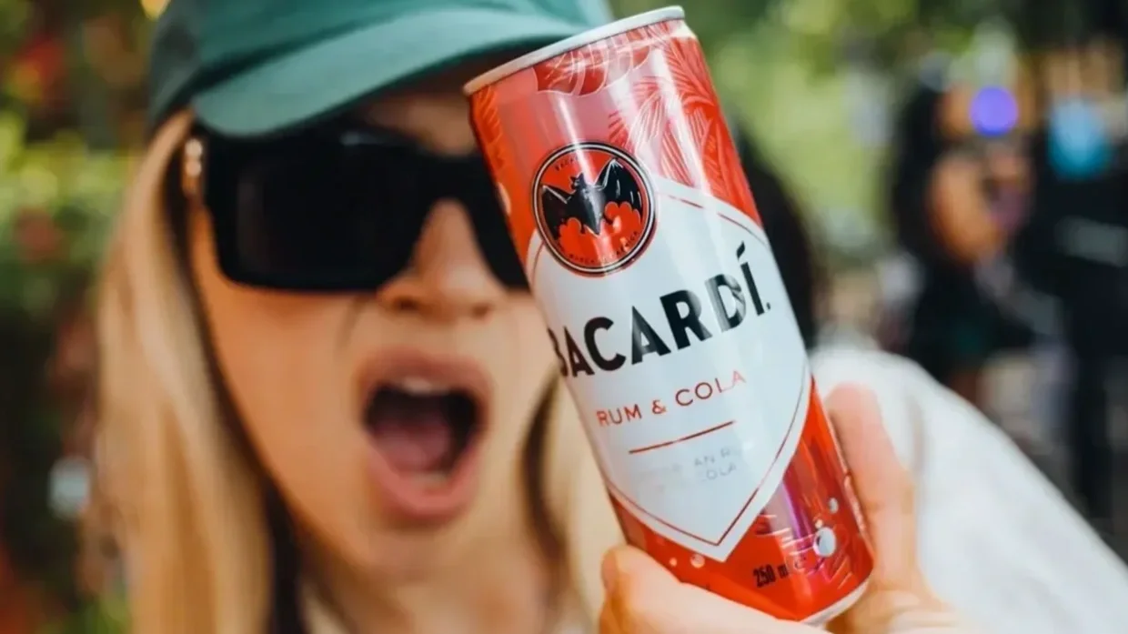  Person holding a Bacardí Rum &amp; Cola ready‑to‑drink can in an outdoor setting, showcasing bold red and white branding, premium rum mixed drink credentials and vibrant lifestyle‑focused packaging. 