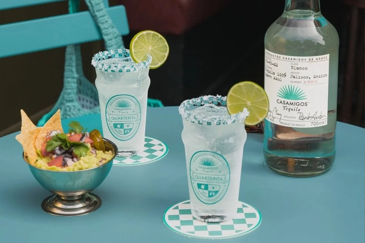 Casamigos Quarterita cocktails served with lime garnishes and chequered salt rims alongside a bottle of Casamigos Blanco Tequila and Mexican-inspired bar snacks, showcasing a refreshing tequila serve in a vibrant hospitality setting.
