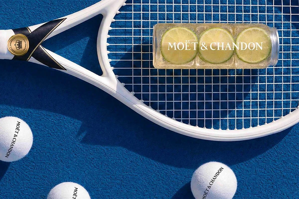 Moët & Chandon branded tennis balls, racket and Champagne-inspired serve presented on a blue tennis court, highlighting the luxury Champagne brand’s partnership with the US Open.