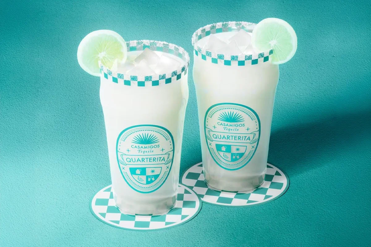 Two Casamigos Quarterita cocktails served over ice in branded glasses with lime wheel garnishes and chequered salt rims, styled against a turquoise backdrop to showcase a refreshing tequila cocktail serve.