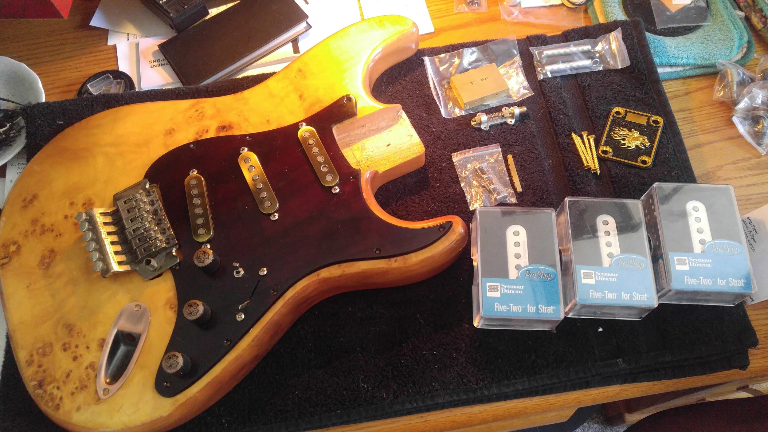 Loose test fit of some of the components, including brass knobs and pickup covers, copper output jack, old Floyd Rose tremelo, brass replacement block for tremelo, Trem Blocker unit for tuning stability, custom brass neckplate, wood pickguard and a …