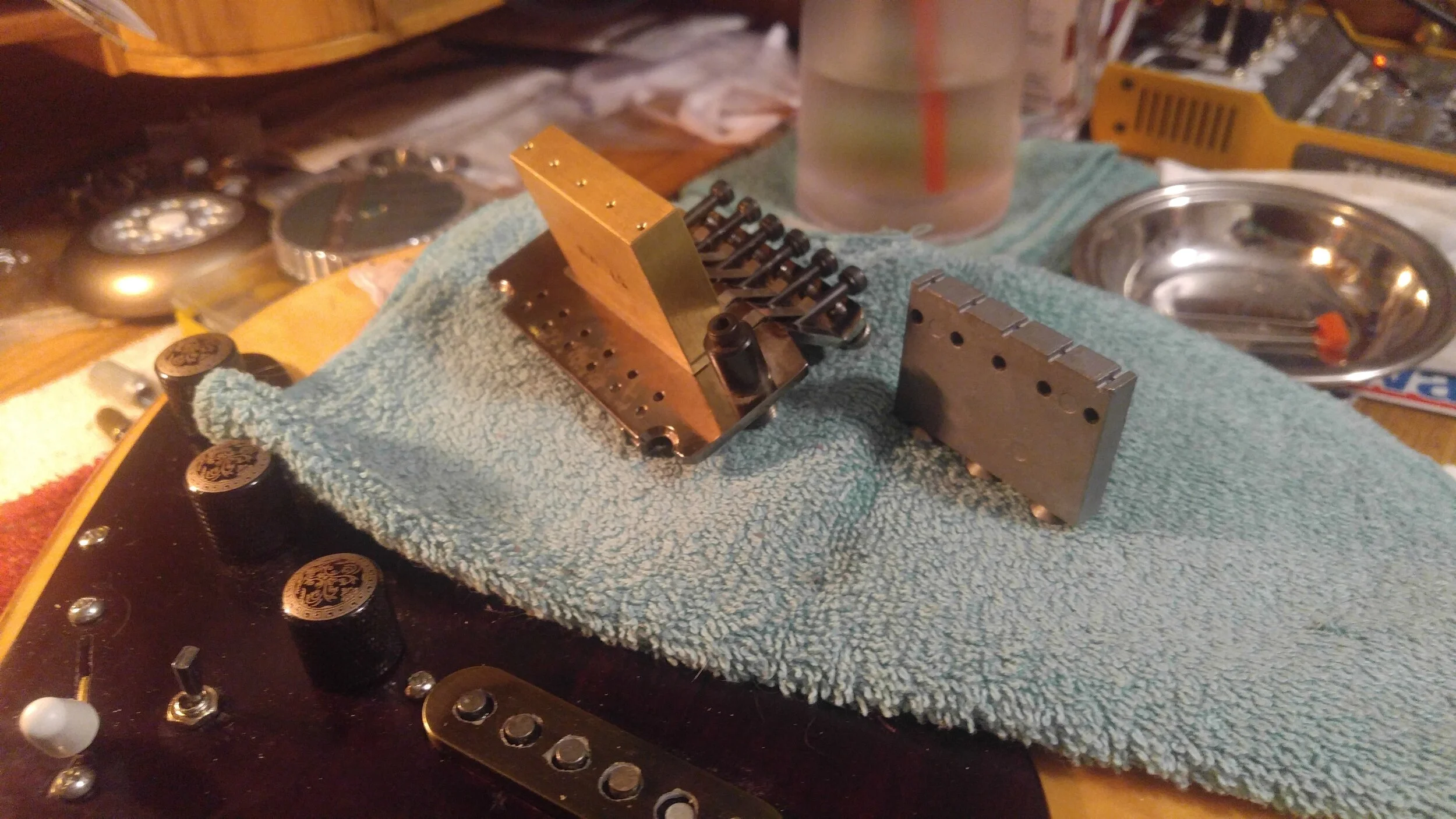 Closeup of brass tremelo block replacement, and original factory unit.