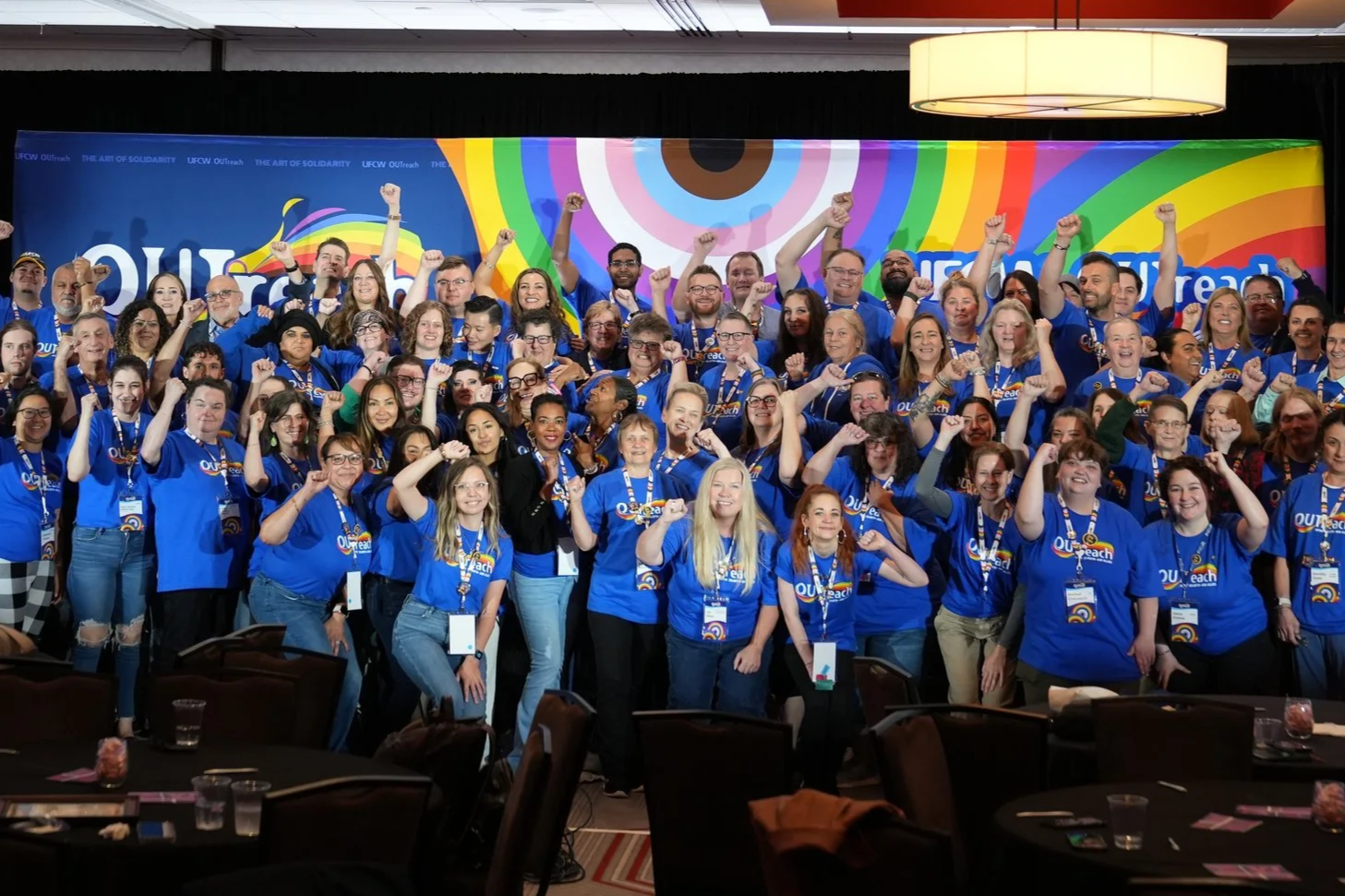 Photo of UFCW OUTreach members standing together for a group photo with their fists raised in the air and wearing matching UFCW OUTreach shirts.