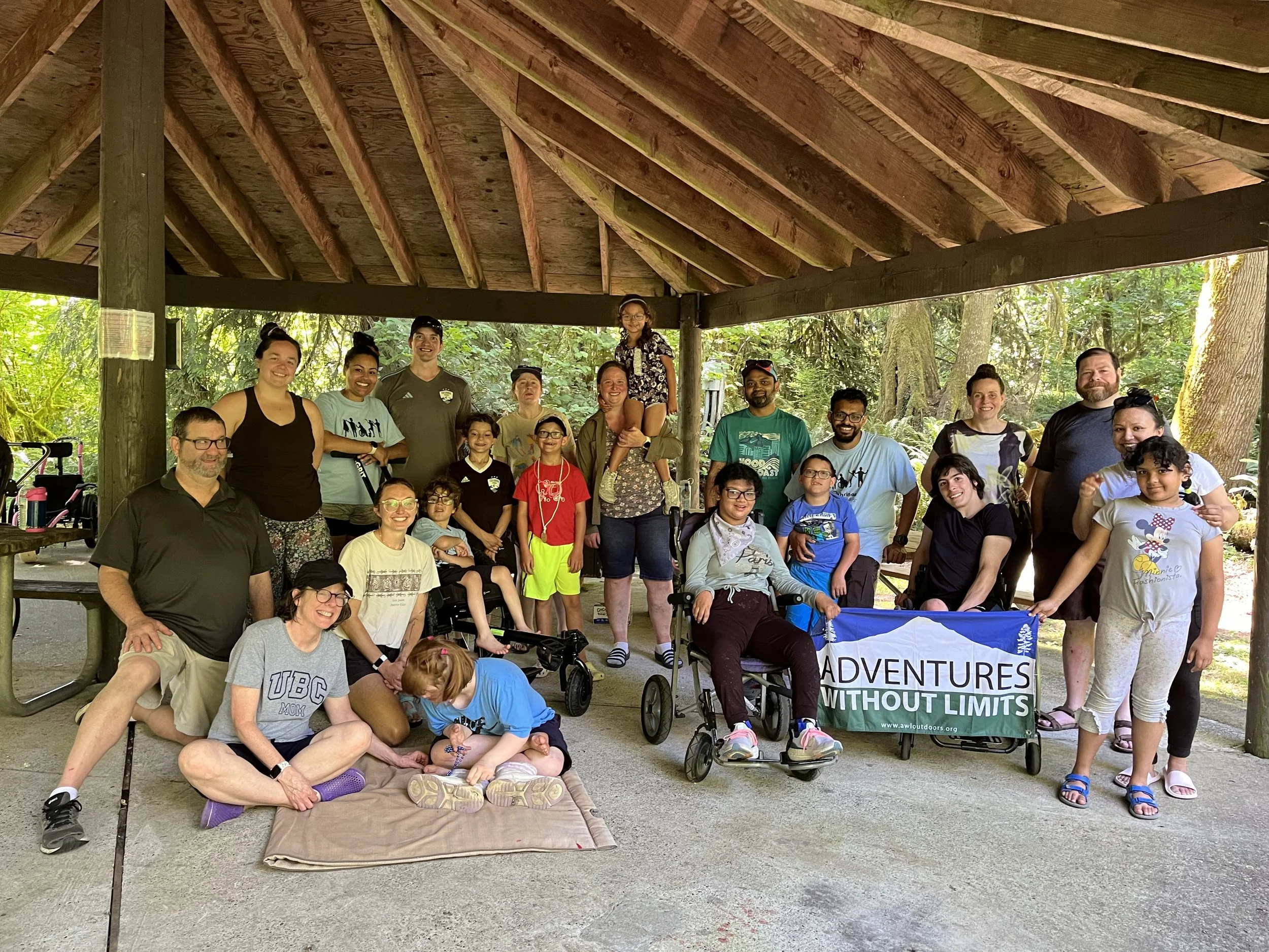 A group of kids and families pose for a photo under a picnic shelter during a weekend camping program