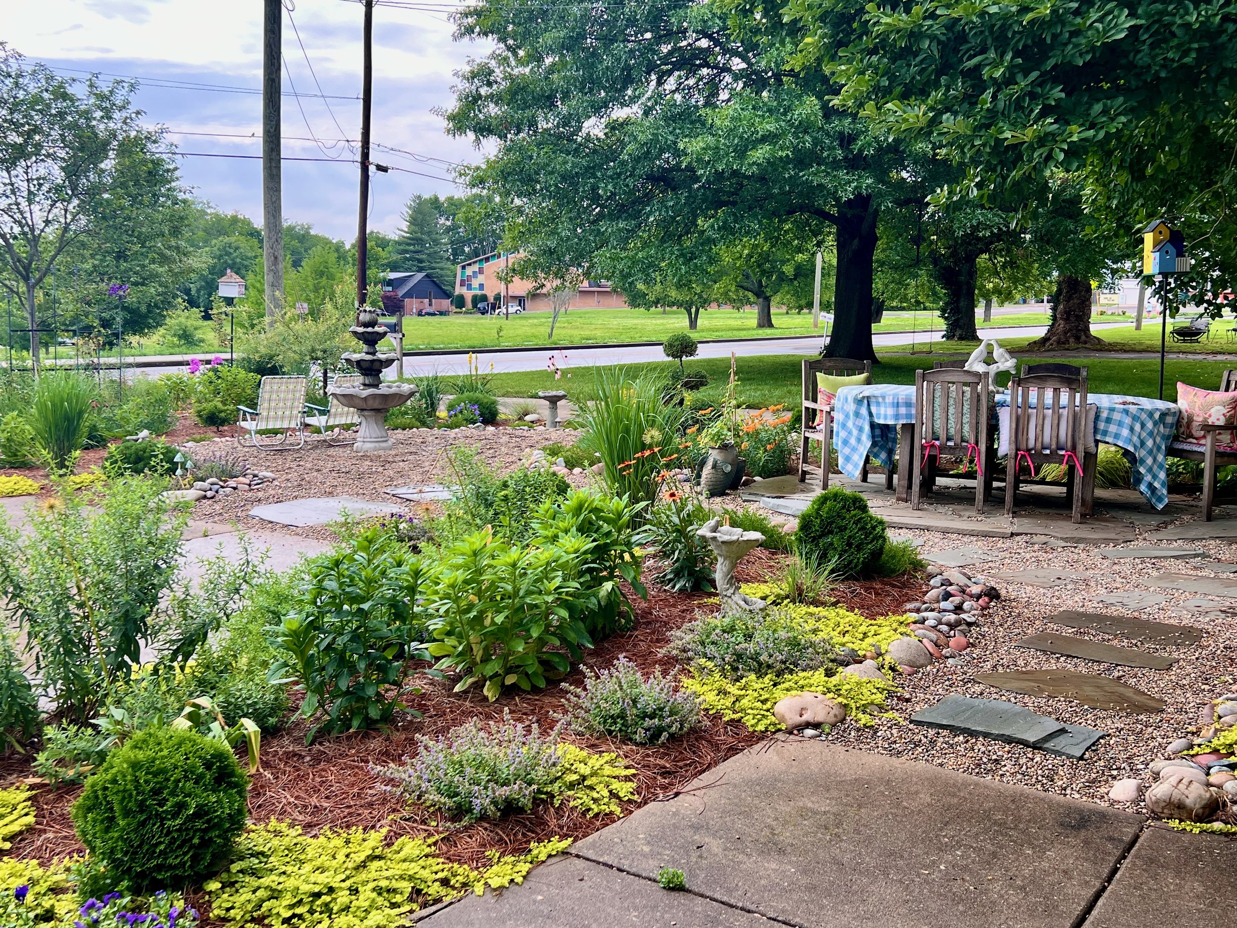 A lawnless front yard pollinator garden in Nashville, TN, designed by The Grass Girl, with a fountain, bird baths, native pollinators plantings, and a dining table.
