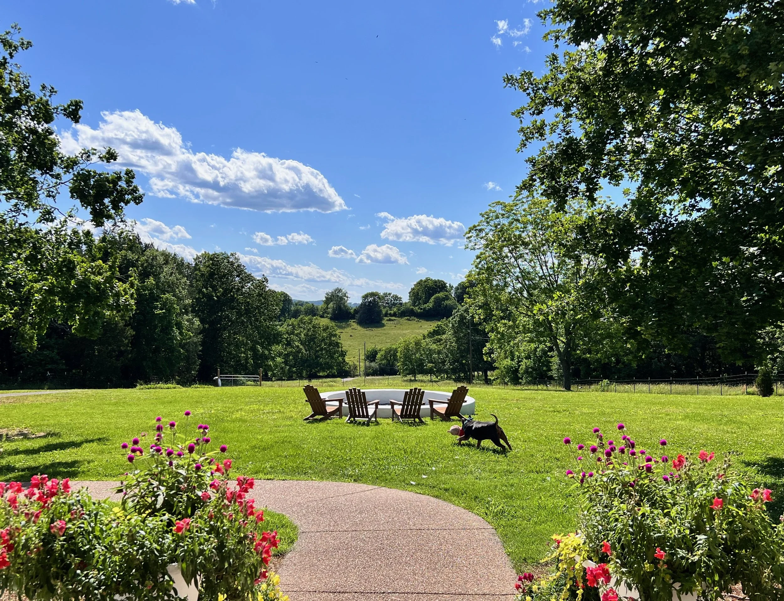 Custom fire pit with Adirondack chairs surrounded by pollinator garden at midday, middle Tennessee farm designed by The Grass Girl