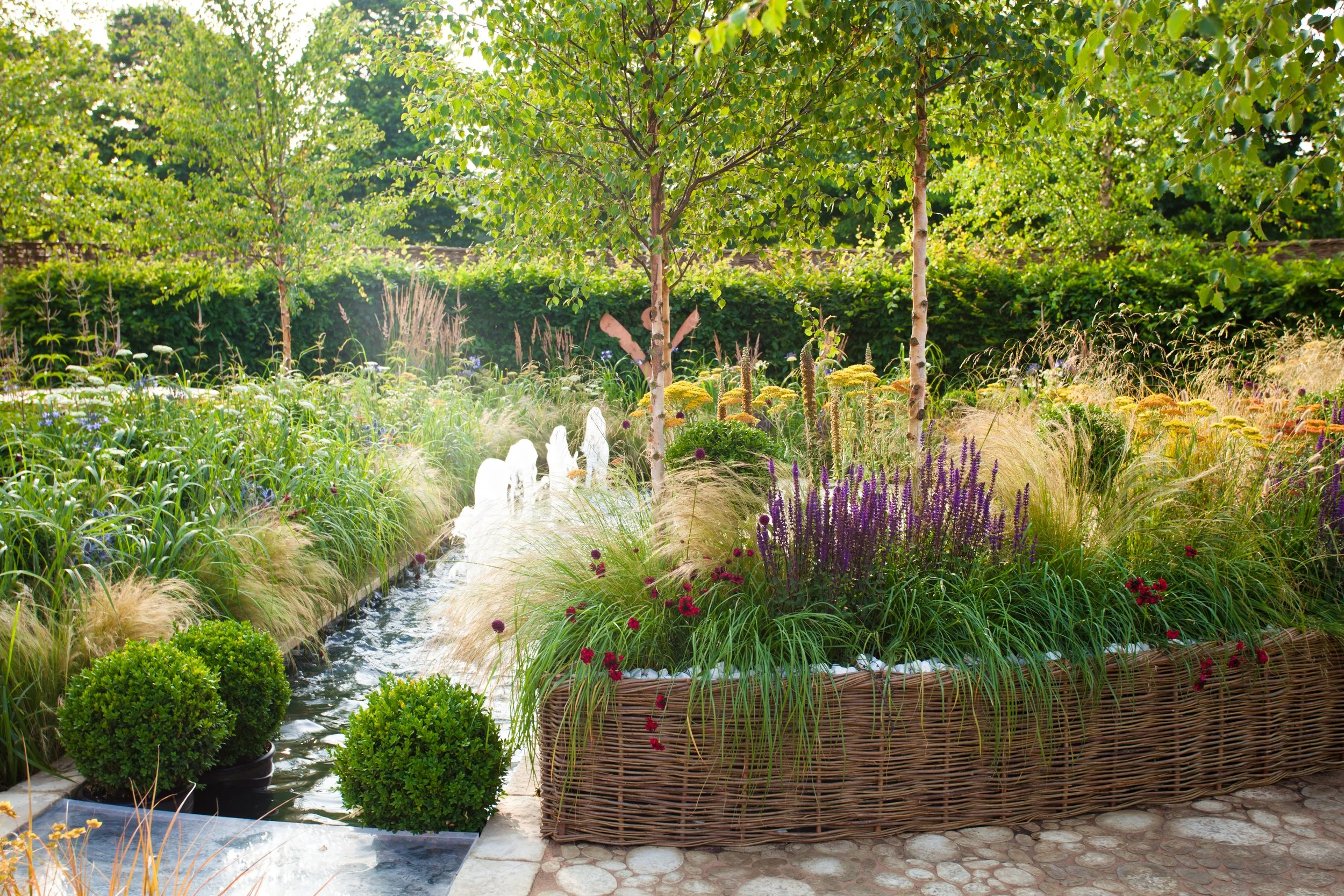 A gorgeous water feature in the middle of a raised planter bed system in a well designed garden