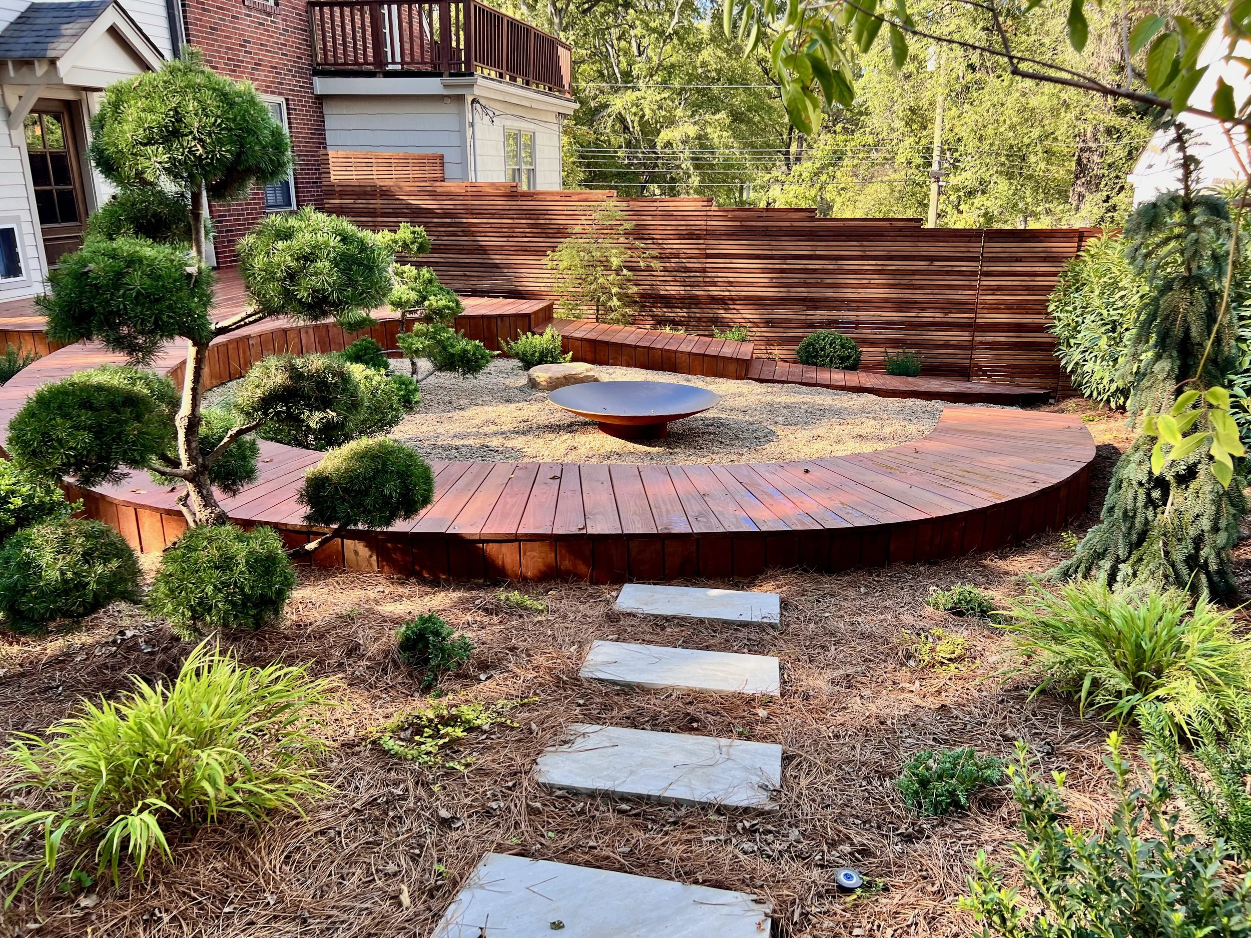 A Japanese inspired back yard with a circular deck, metal fire pit, and topiary specimens designed by The Grass Girl, a TN garden designer.
