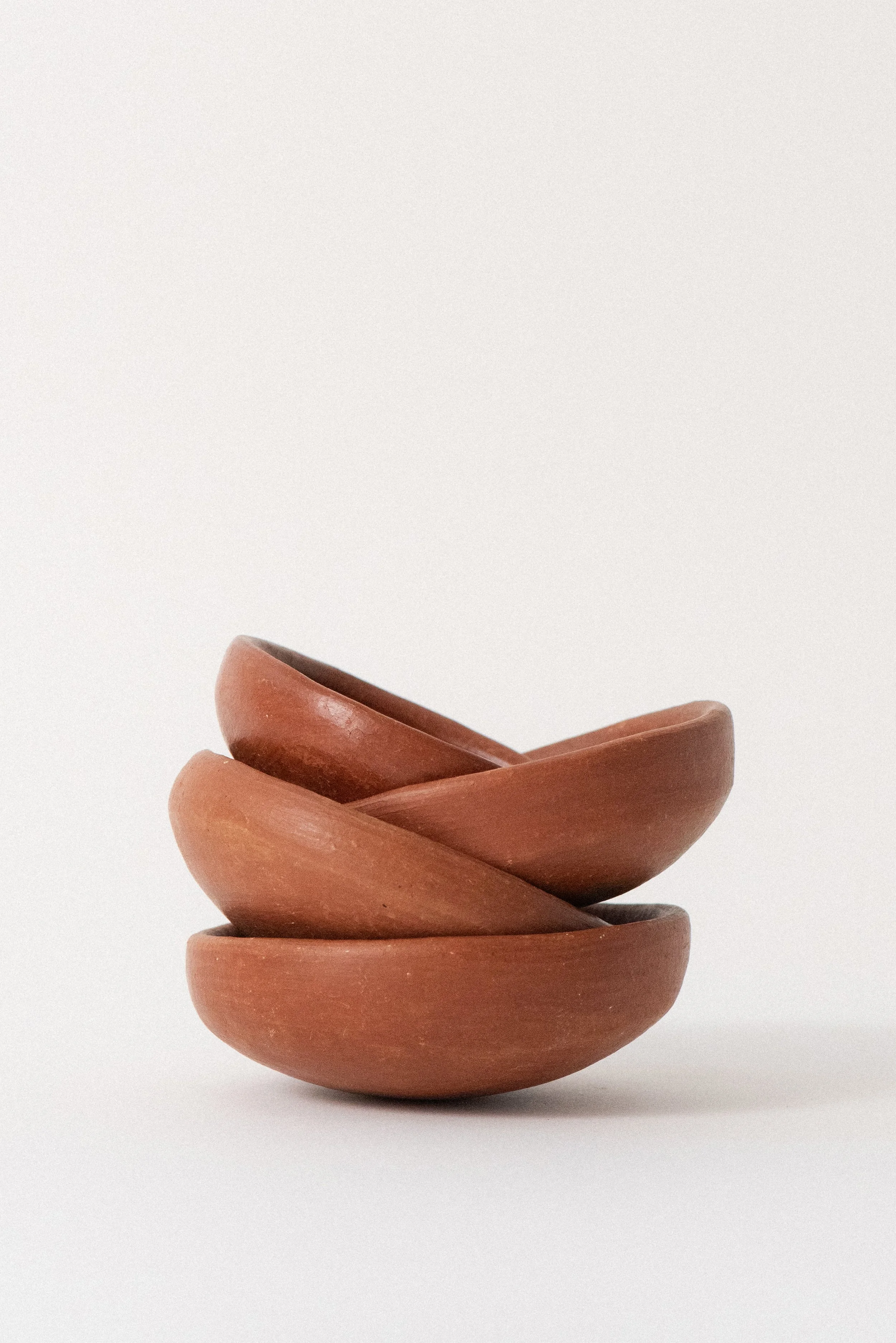 Stack of handmade barro rojo red clay bowls from Oaxaca, Mexico, displayed against a clean white background — rustic, artisanal kitchenware.