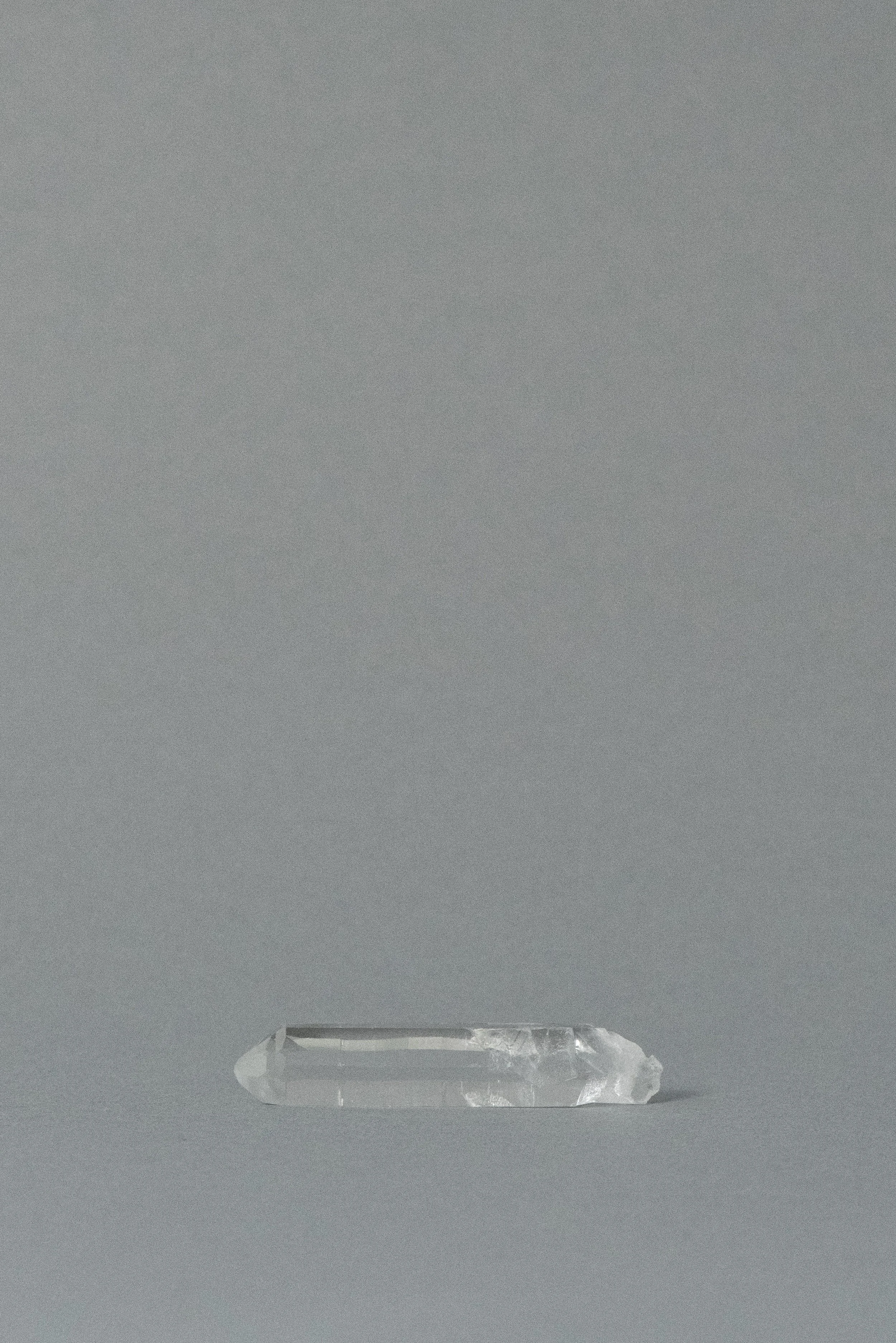 Transparent clear quartz point from Brazil, single-terminated and polished, shown on a minimalist gray background.