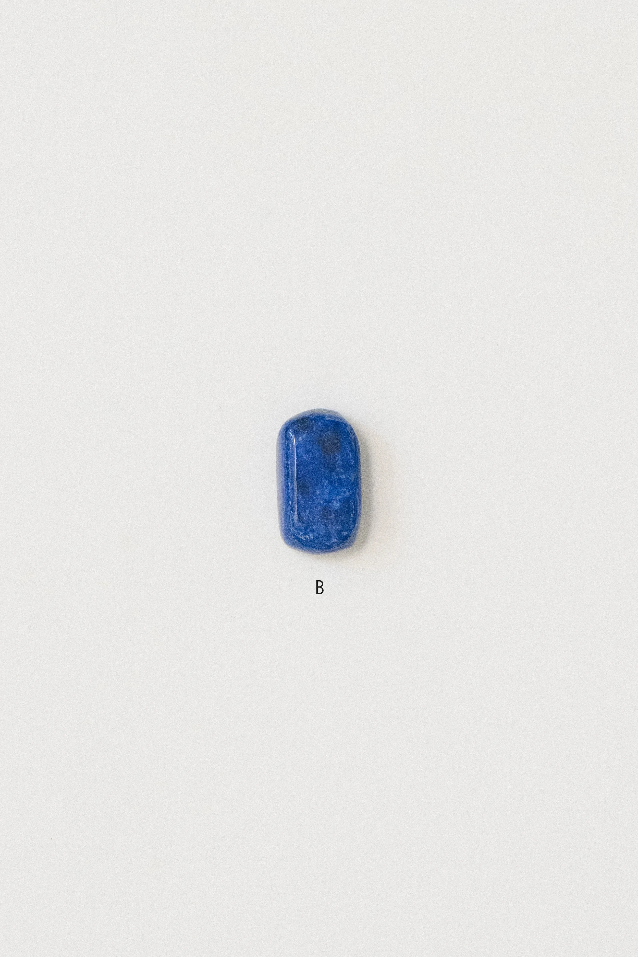 Single polished lapis lazuli stone from Afghanistan labeled 'B' on a white background, featuring a rounded rectangular shape and rich blue color.