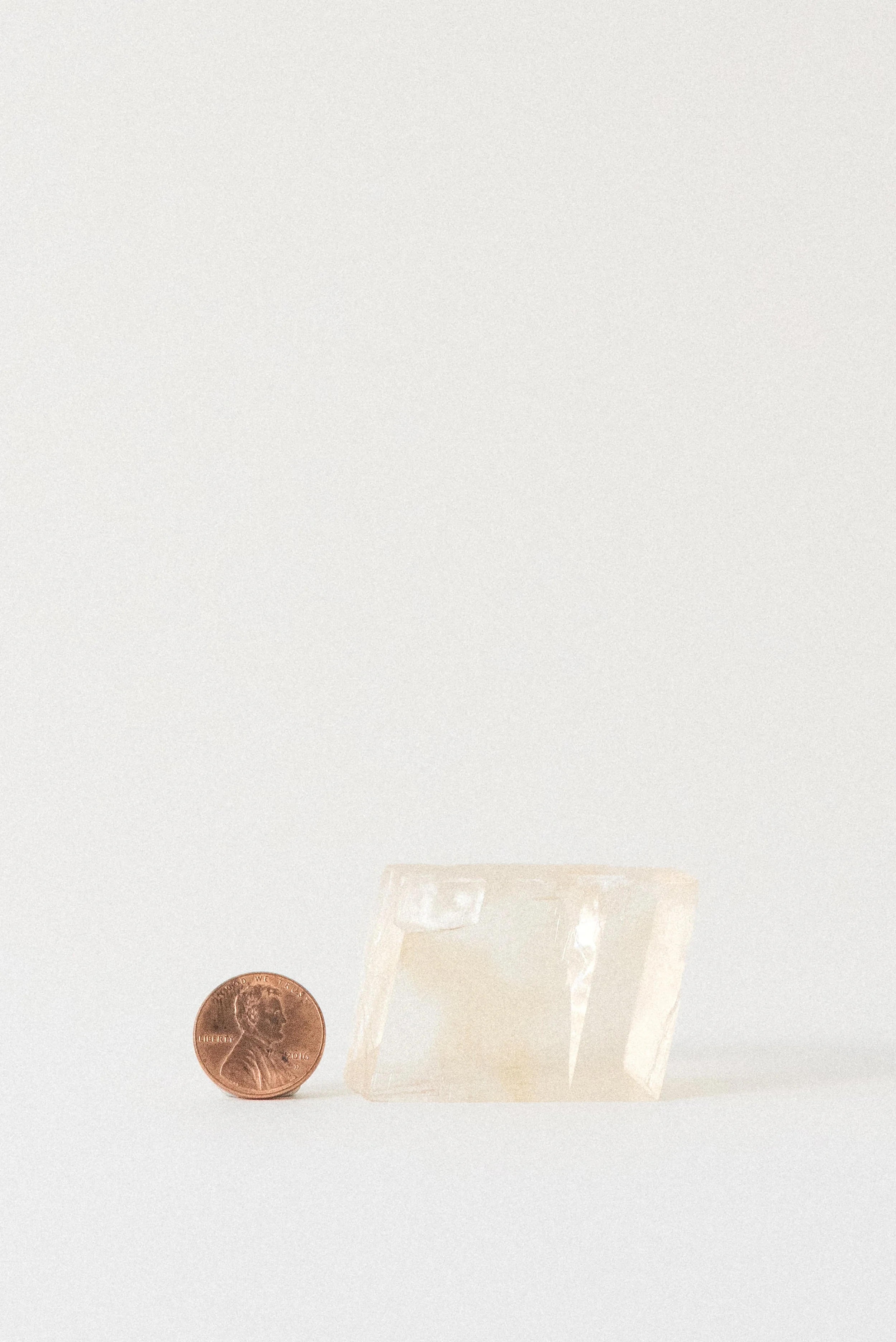 Yellow calcite rhomboid from Aurangabad, India, shown with a U.S. penny for scale on a white background under soft studio lighting
