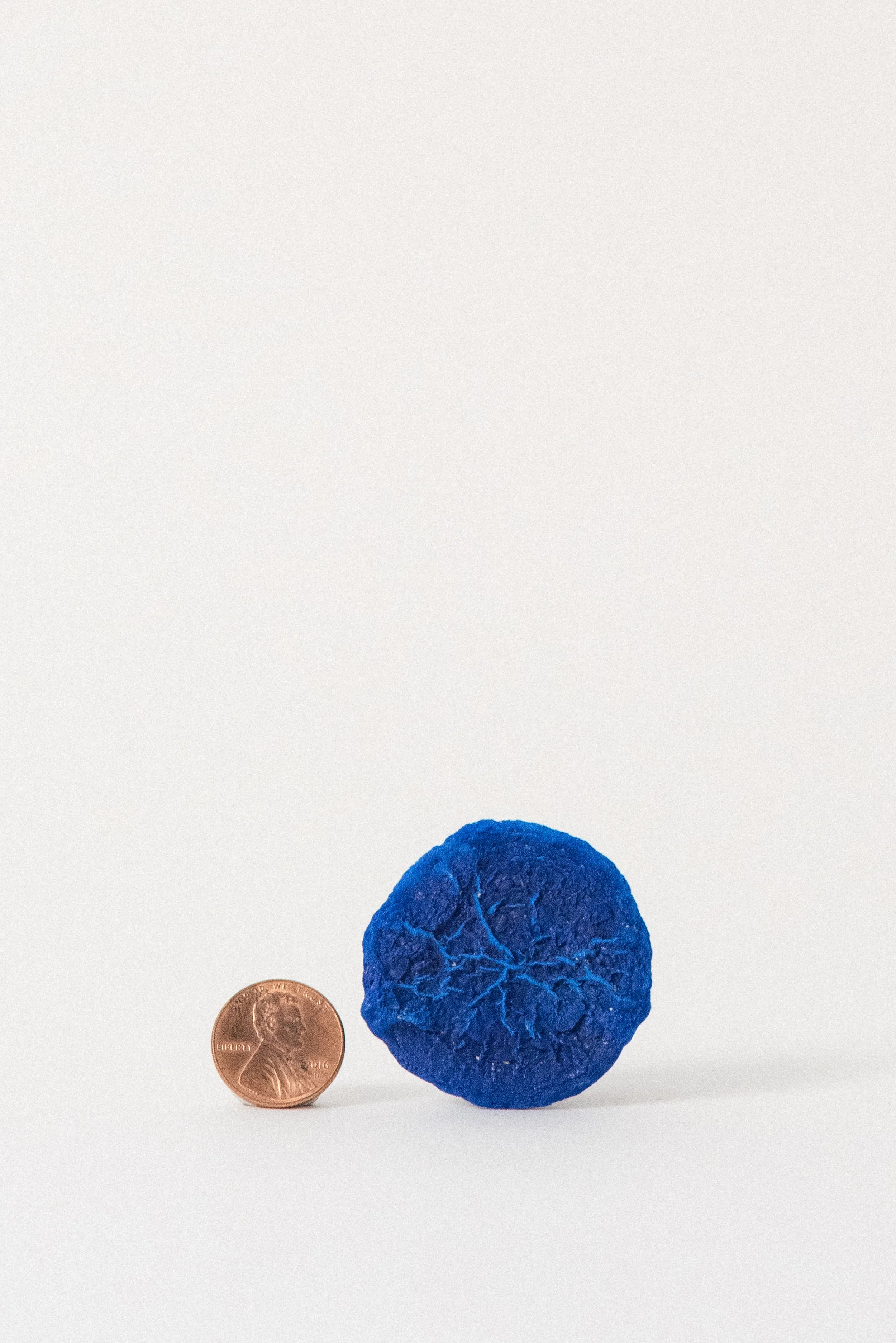 Bright blue azurite sun crystal from the Malbunka Copper Mine in Australia shown next to a penny for scale on a white background.