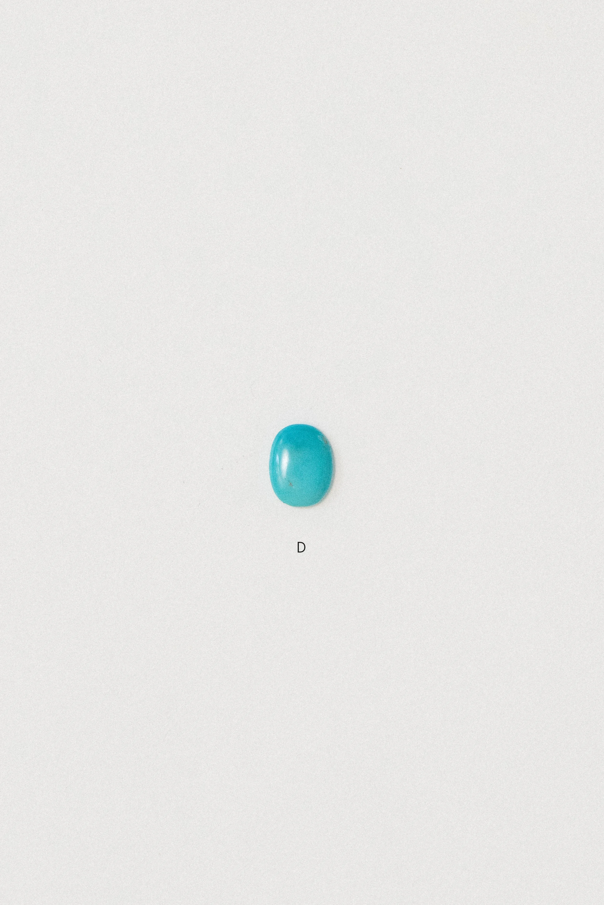 Natural turquoise cabochon from Sinai, Egypt labeled D on a white background.