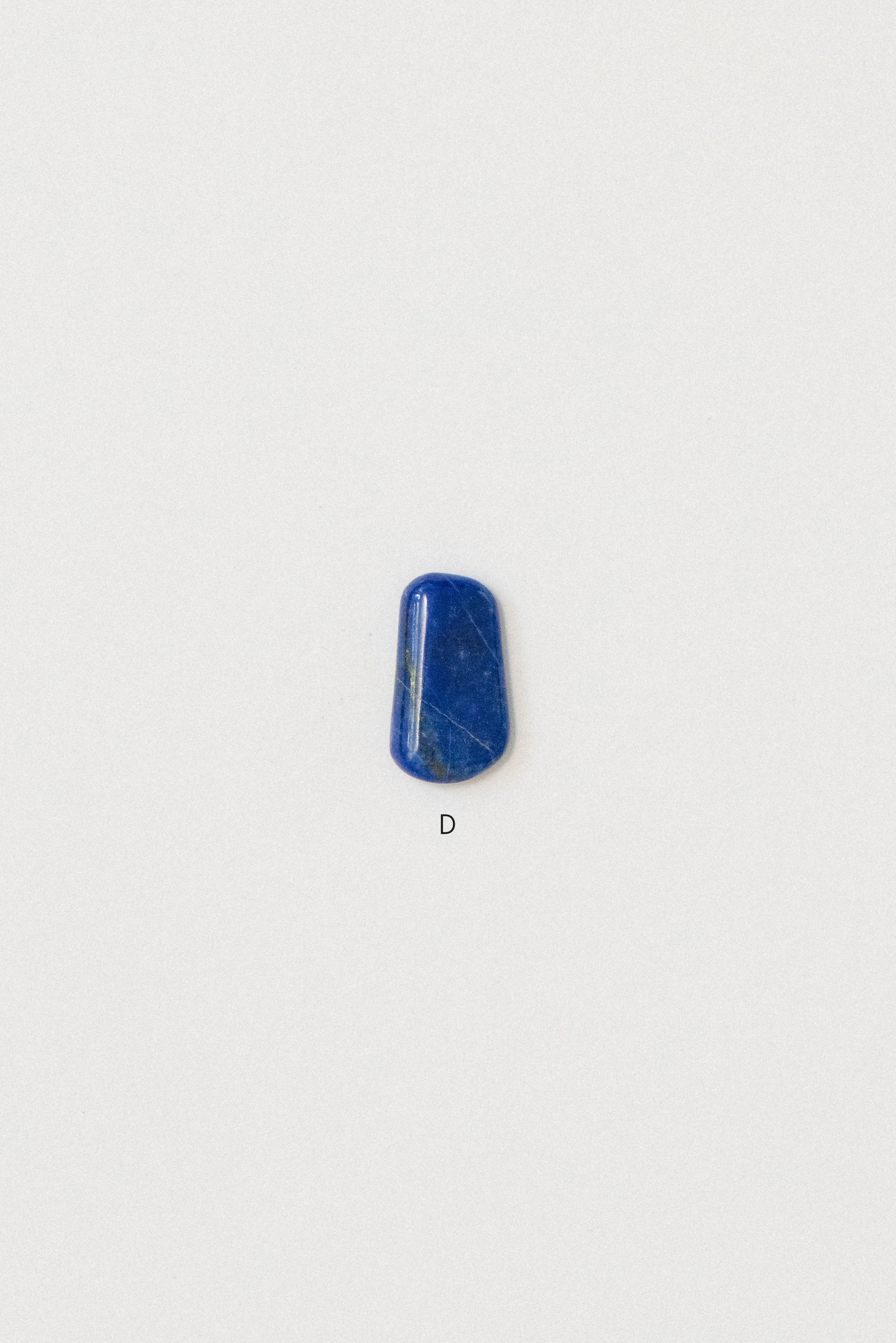 Single polished lapis lazuli stone from Afghanistan labeled 'D' on a white background, featuring a tapered rectangular shape with subtle white veining.
