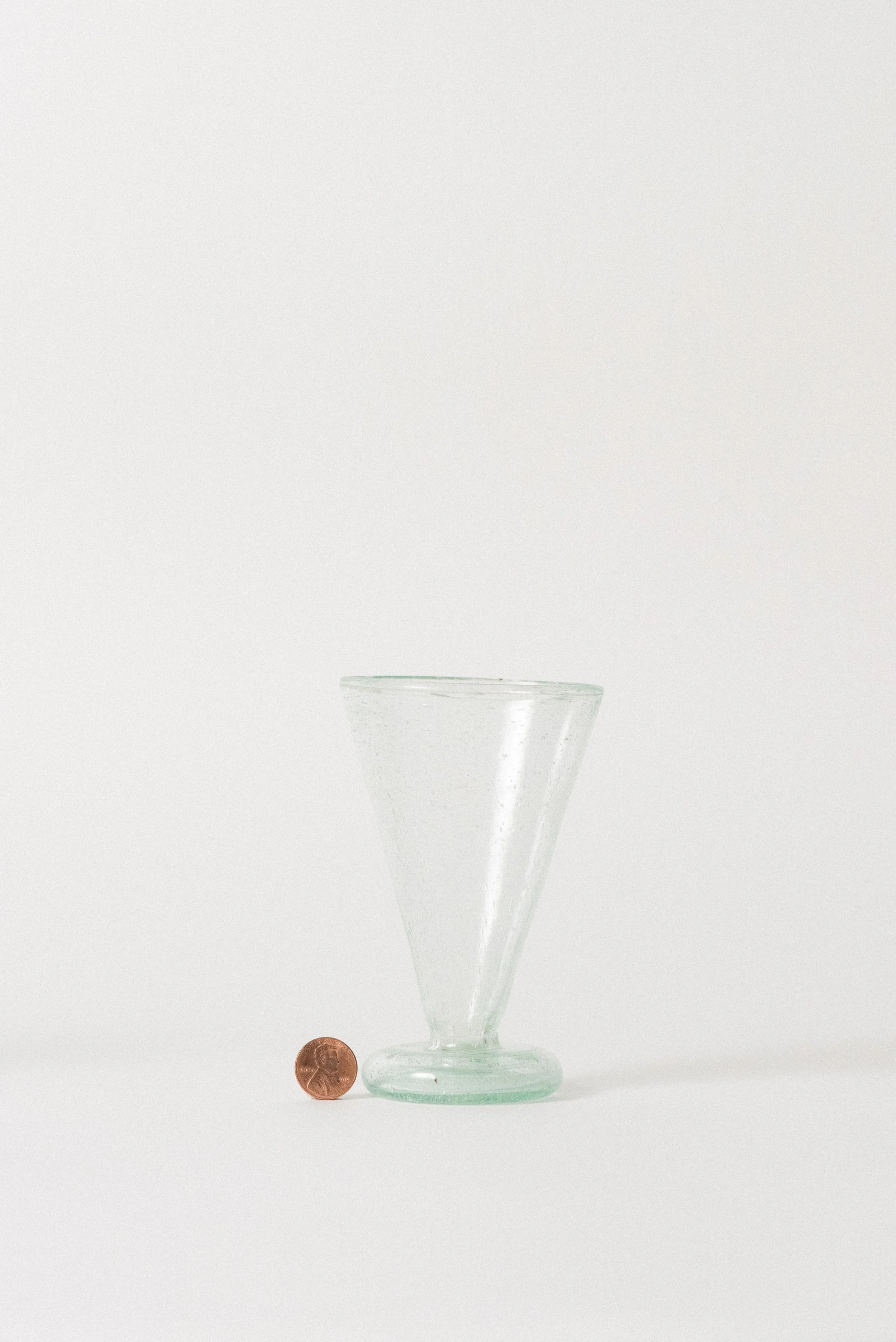 Handblown Egyptian tea glass shown beside a penny for scale, emphasizing petite size and natural seed glass bubbles.